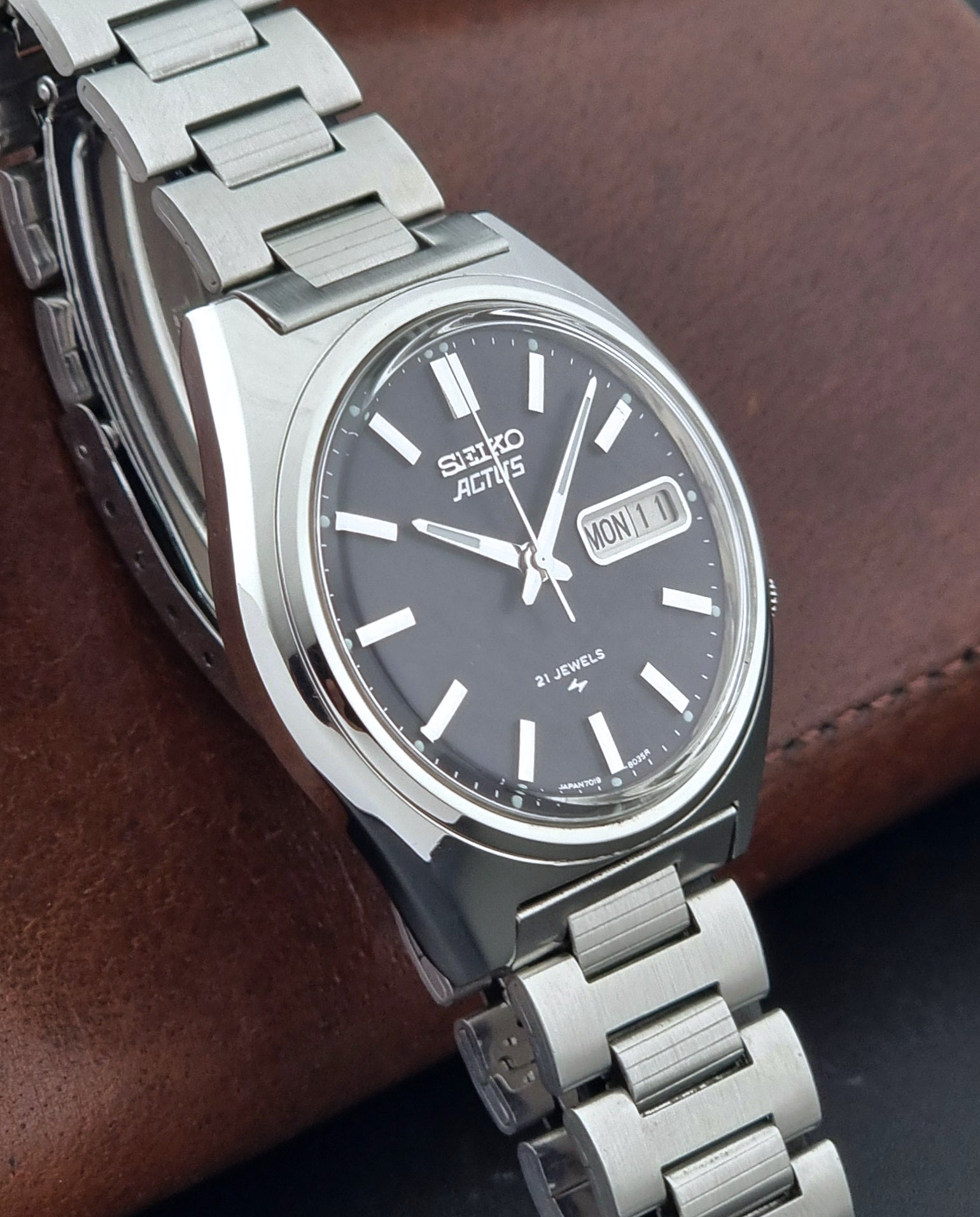 Vintage Seiko Actus Wristwatch 7019-8010 with a Black dial and bracelet on a dark back ground side view