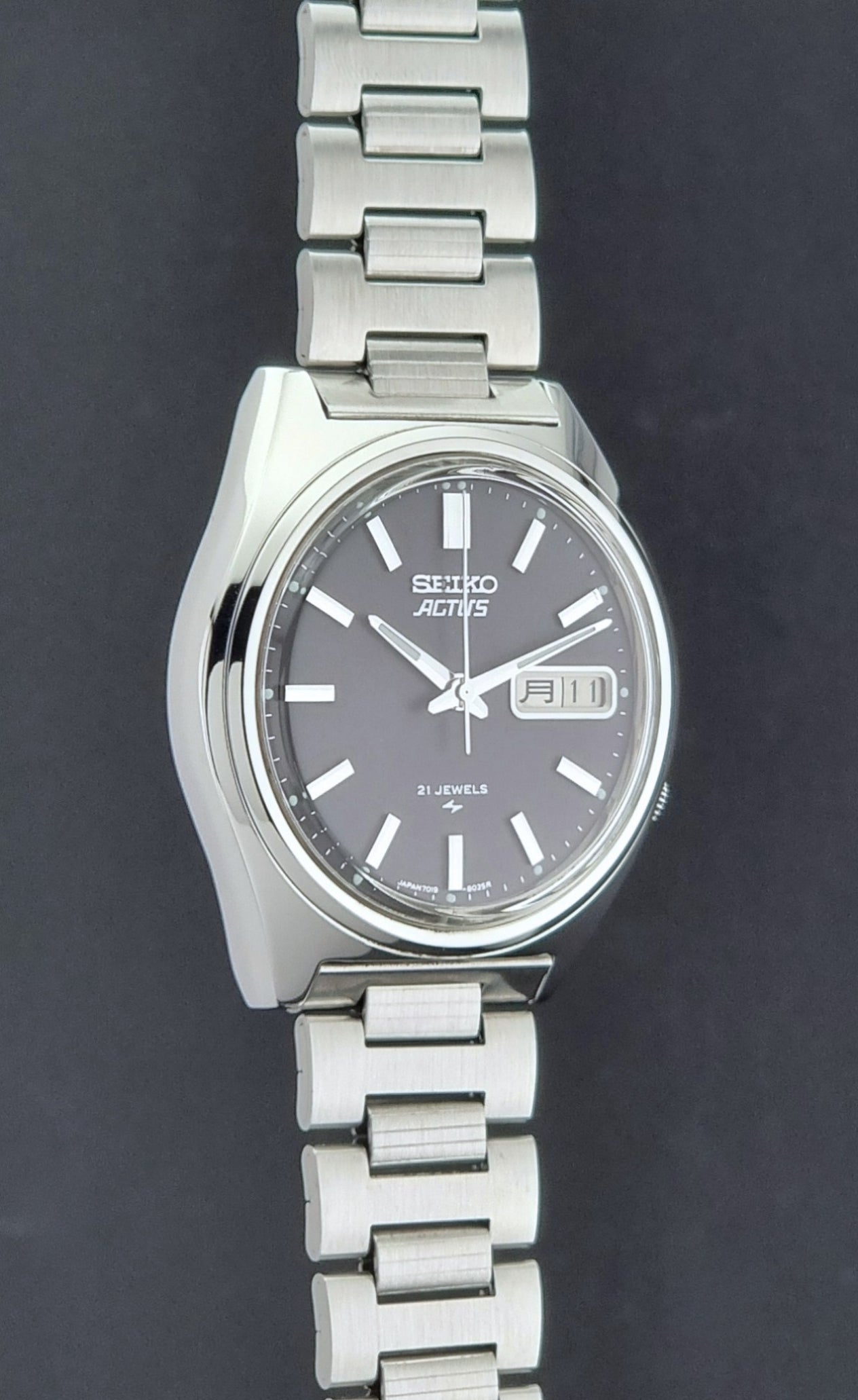 Vintage Seiko Actus Wristwatch 7019-8010 with a Black dial and bracelet on a dark back ground side profile view