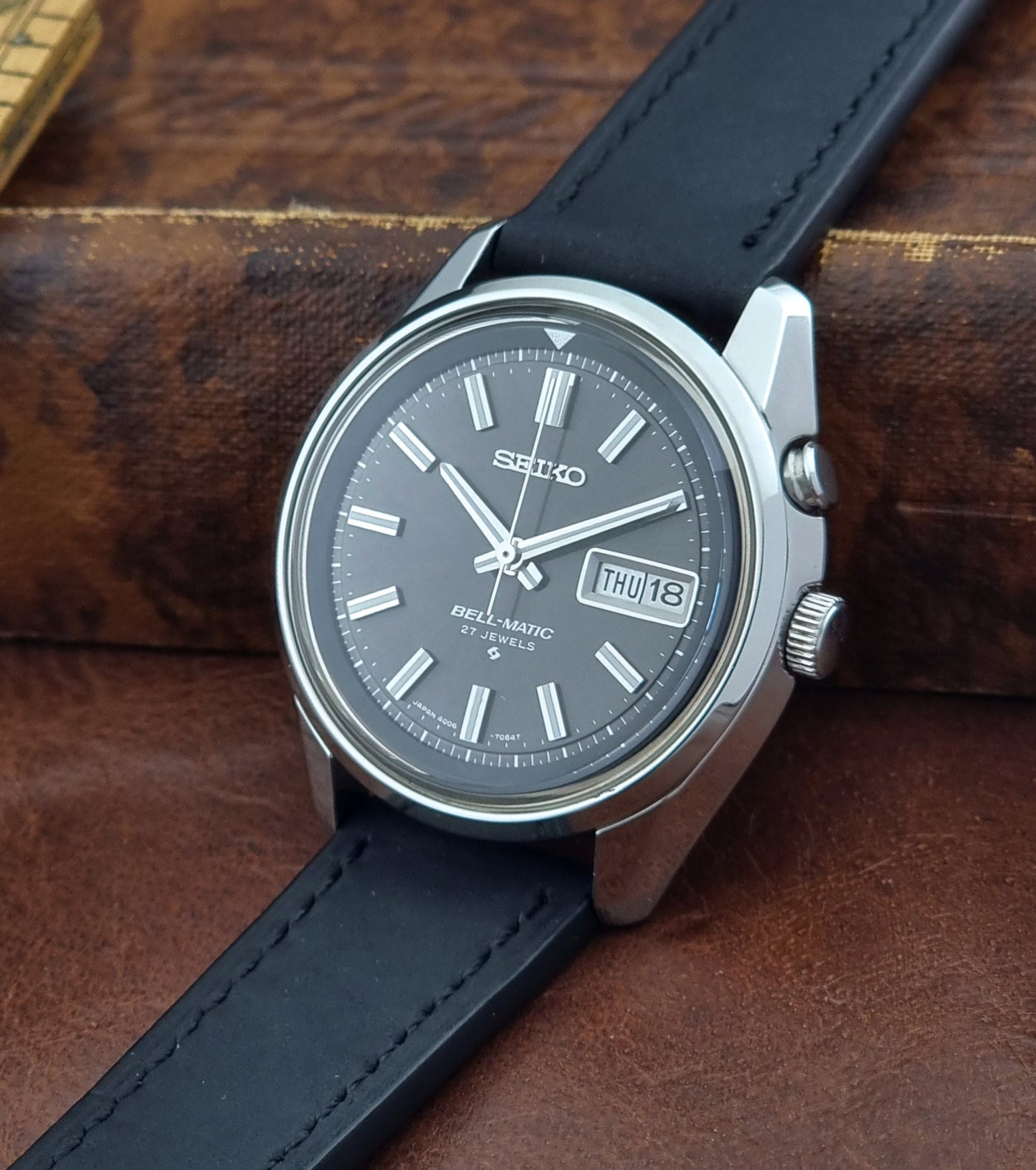 Vintage Seiko Bell-matic Wristwatch with black leather strap on a brown background crown view
