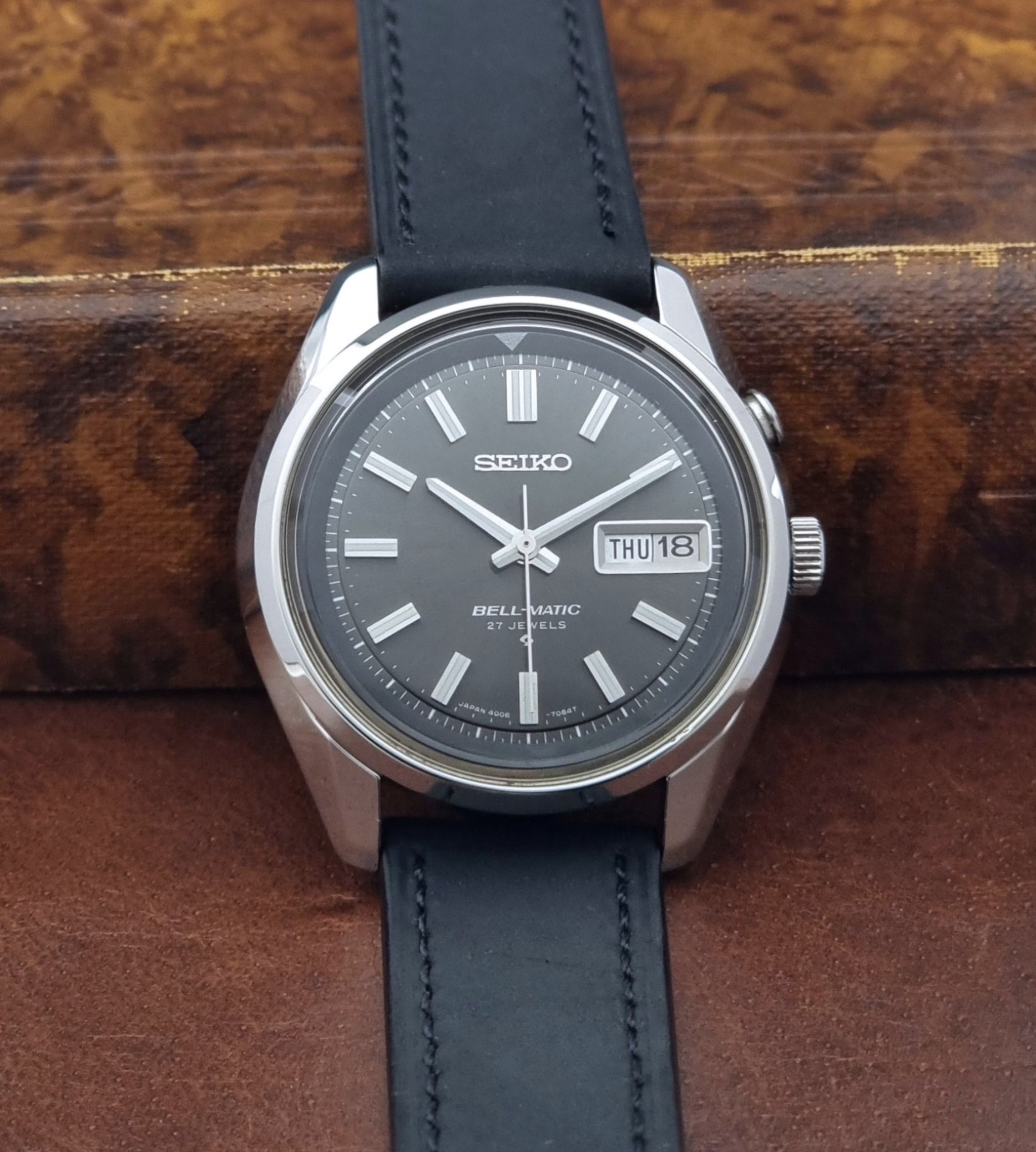 Vintage Seiko Bell-matic Wristwatch with black leather strap on a brown background close front view