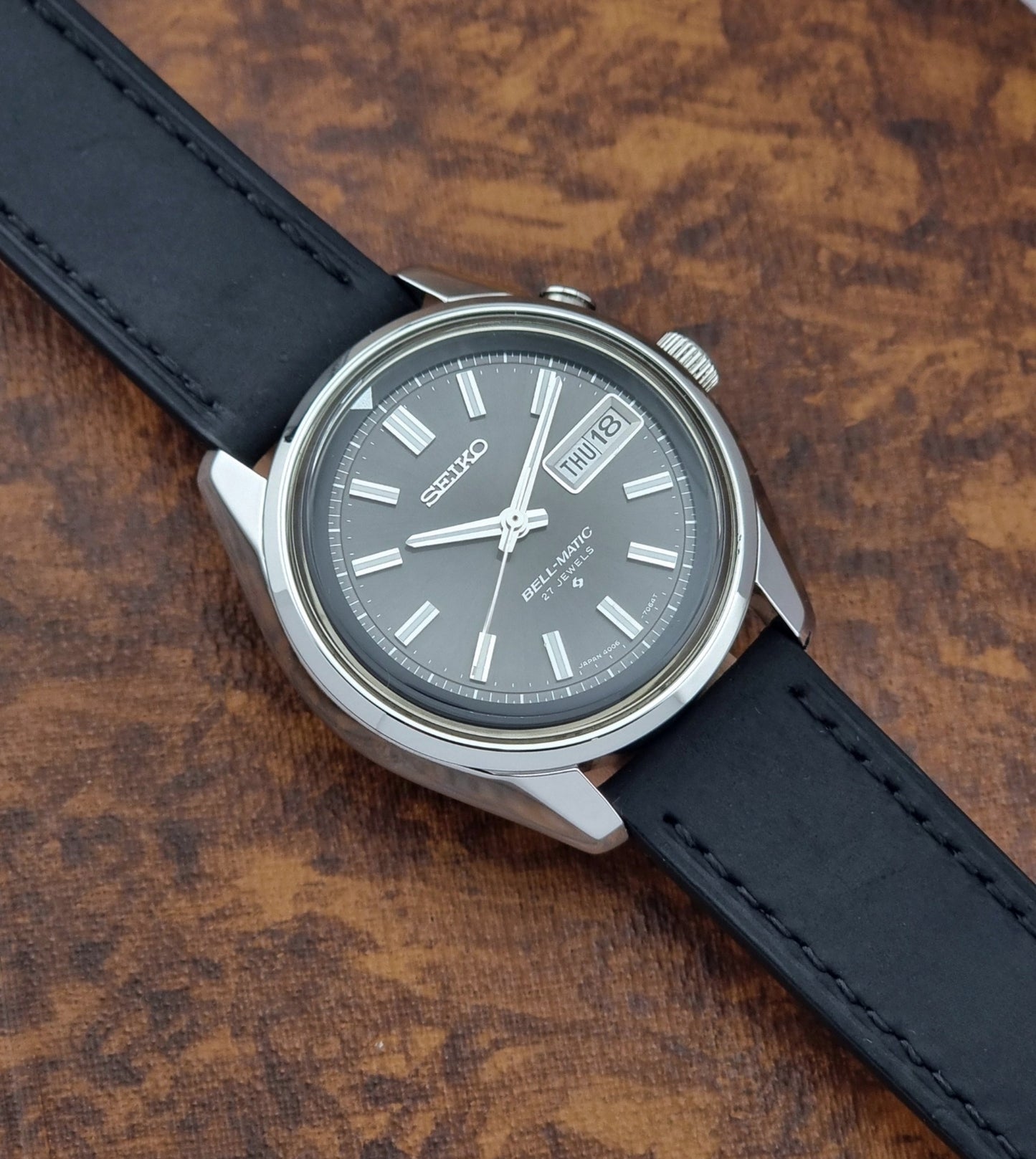 Vintage Seiko Bell-matic Wristwatch with black leather strap on a brown background front view
