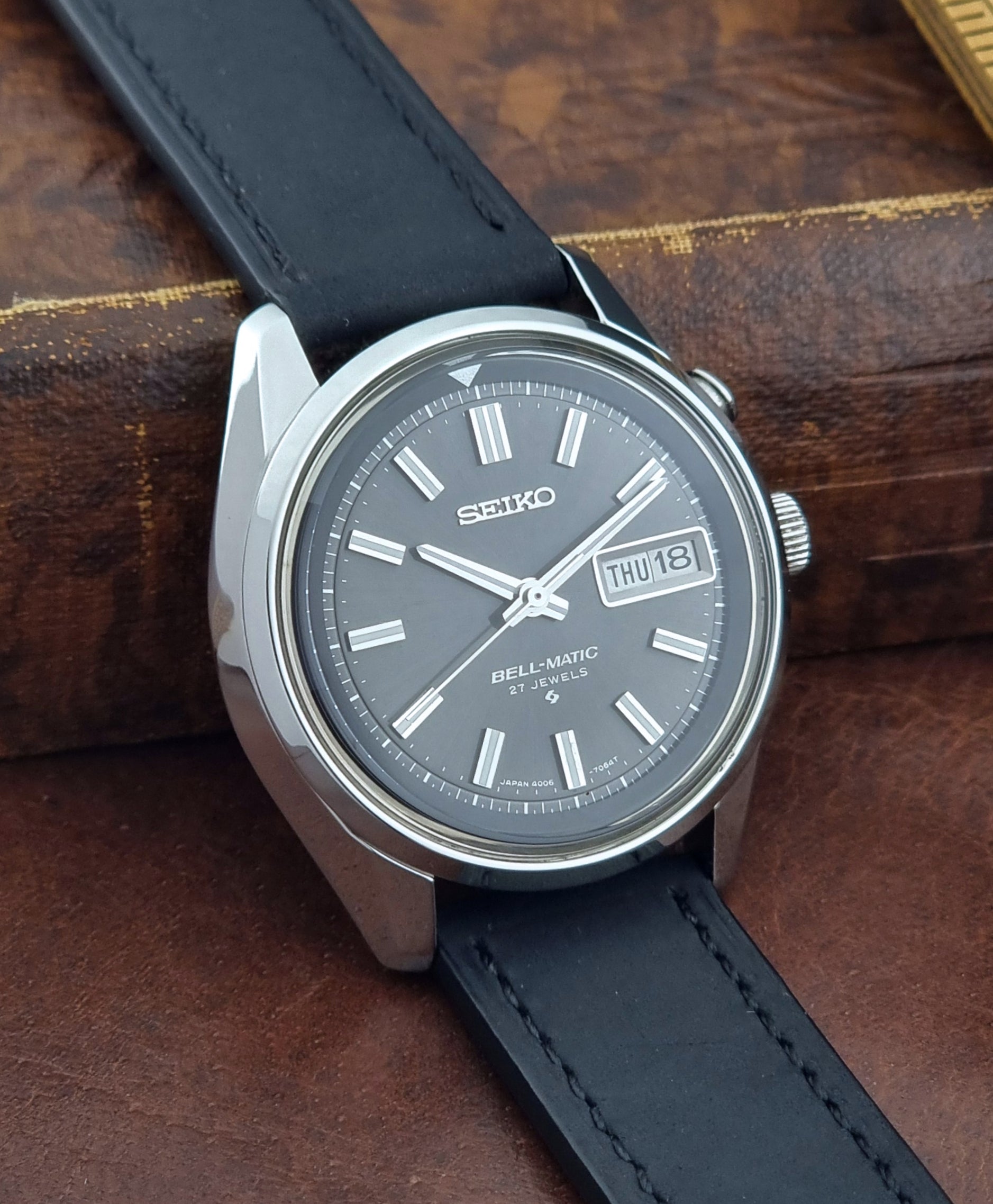 Vintage Seiko Bell-matic Wristwatch with black leather strap on a brown background side view