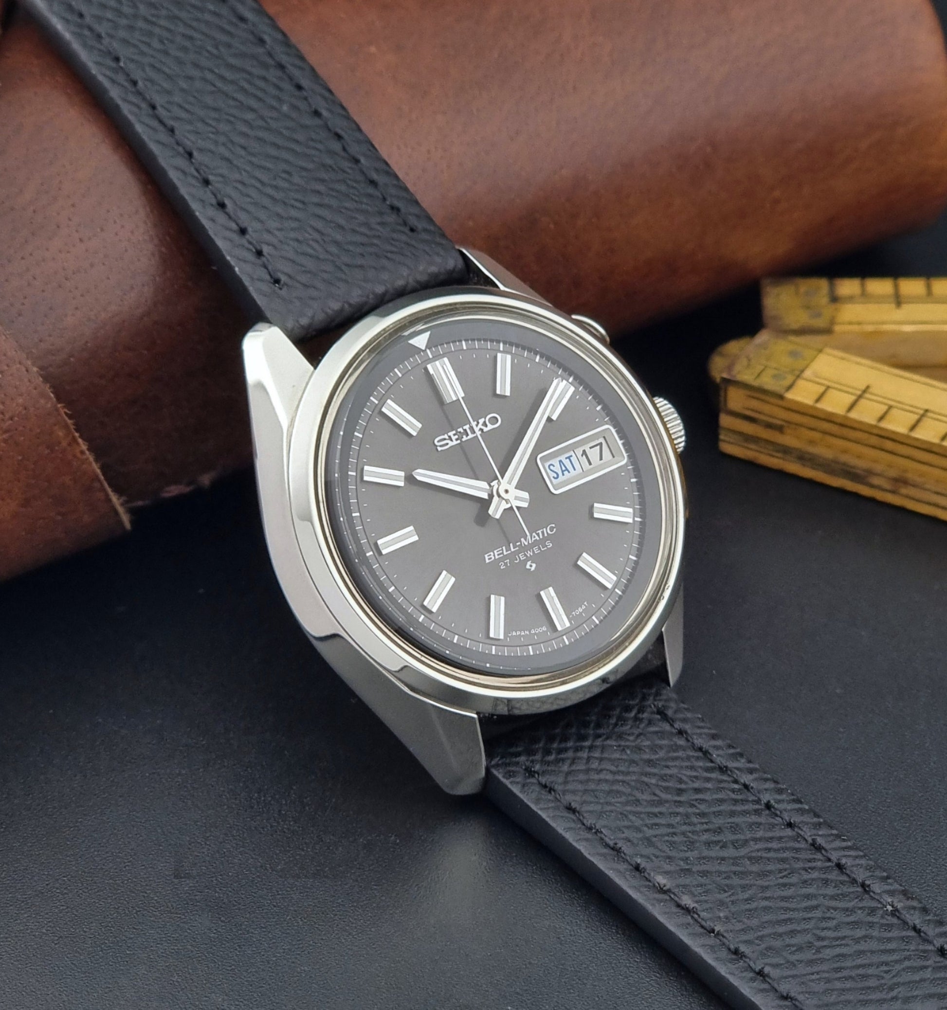 Vintage Seiko Alarm Watch Bell-Matic 4006-7012 with a grey dial and black leather strap on a dark surface side view