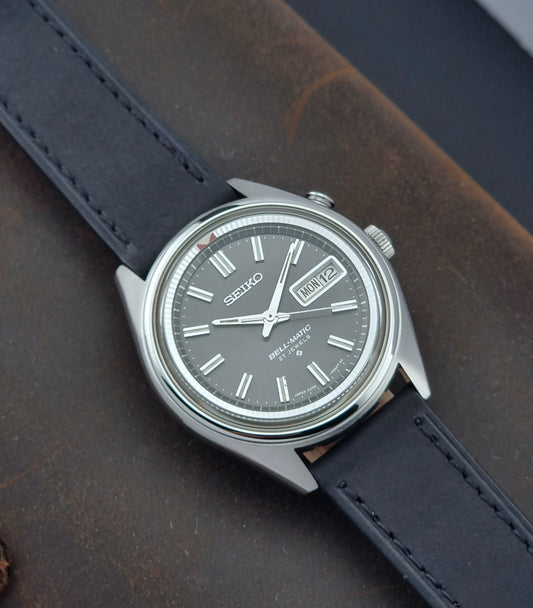 Vintage Seiko Bell-Matic watch with black leather strap on a textured surface