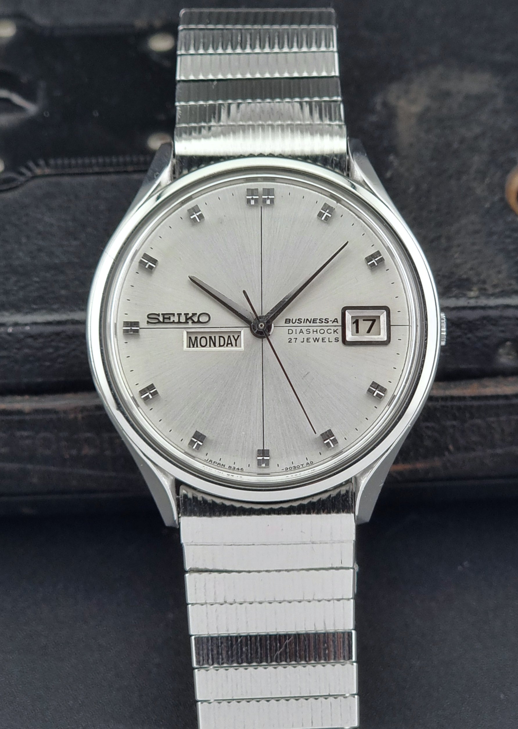 Silver Seiko watch with a white face on a dark textured background