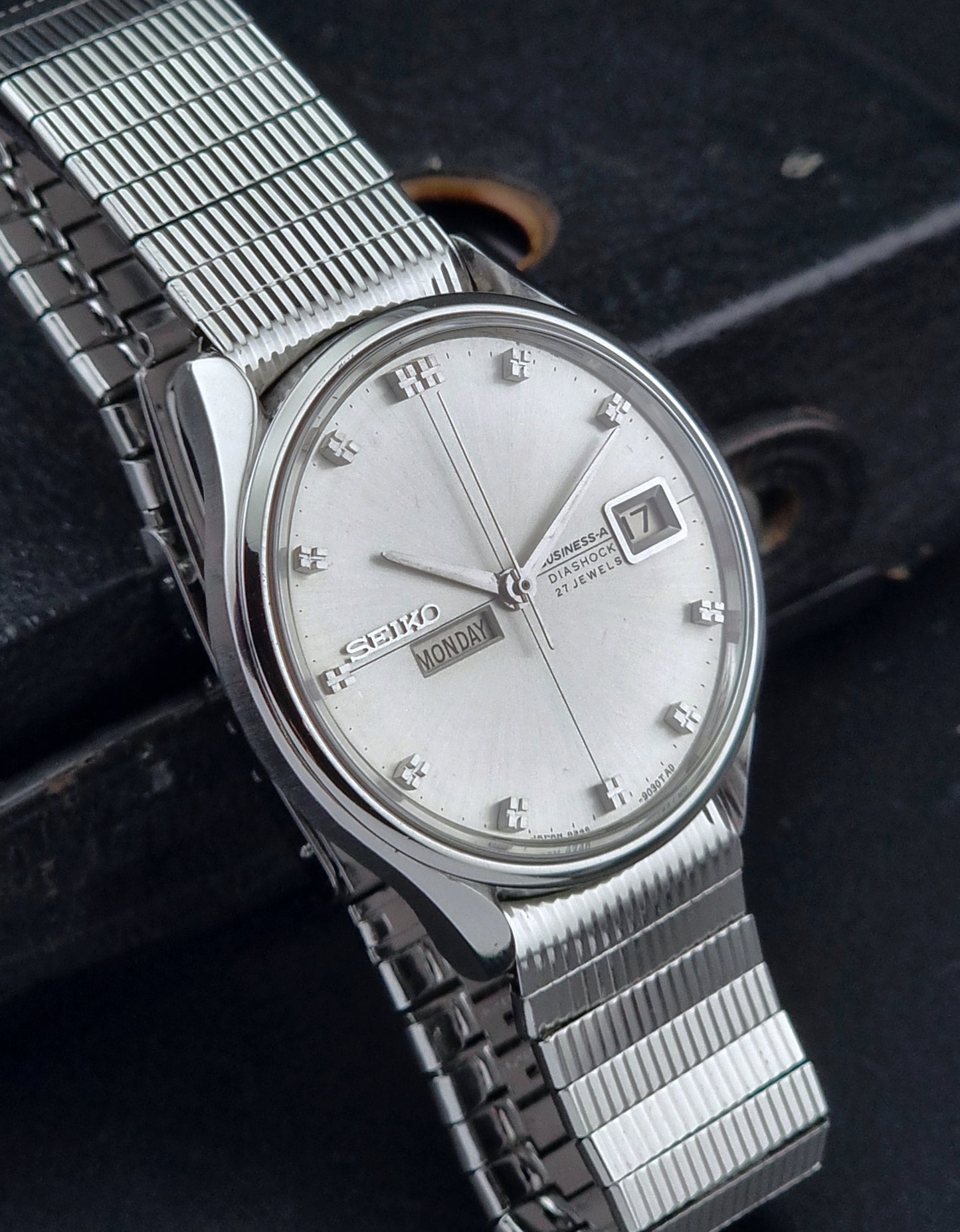 Silver Seiko watch with a mesh band on a dark textured background