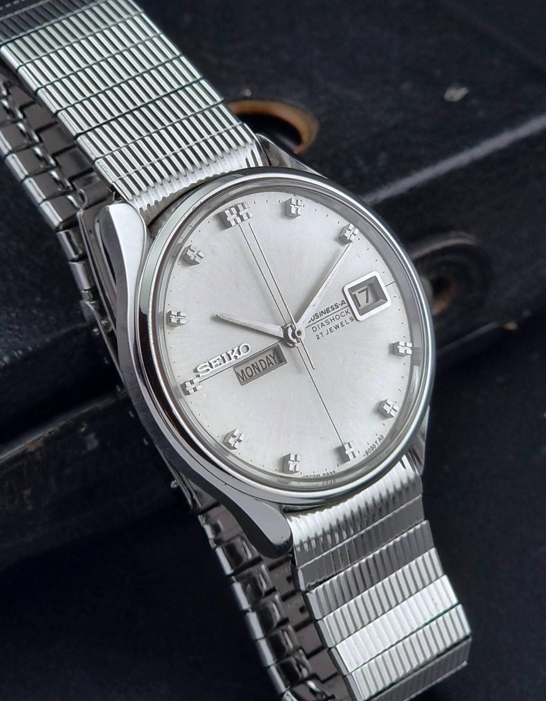 Silver Seiko watch with a mesh band on a dark textured background