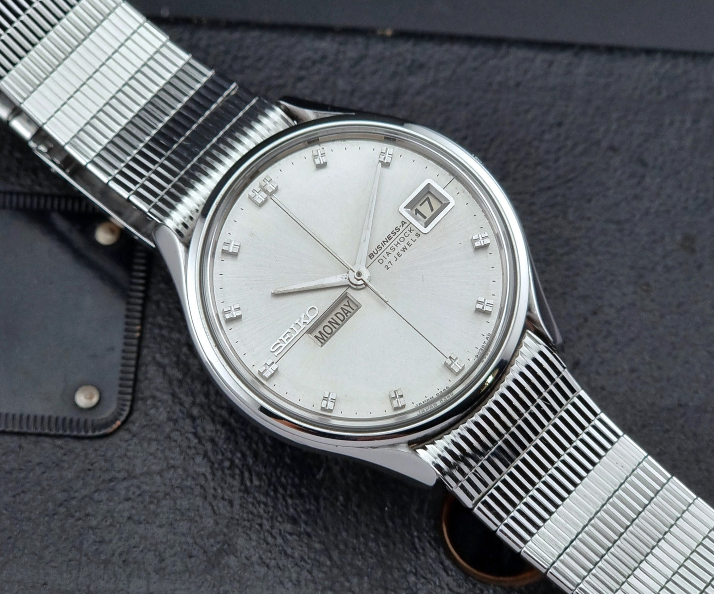 Silver Seiko wristwatch with a detailed face on a textured dark surface