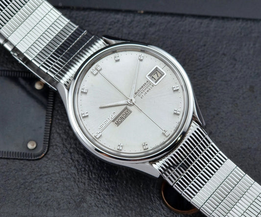 Silver Seiko wristwatch with a detailed face on a textured dark surface