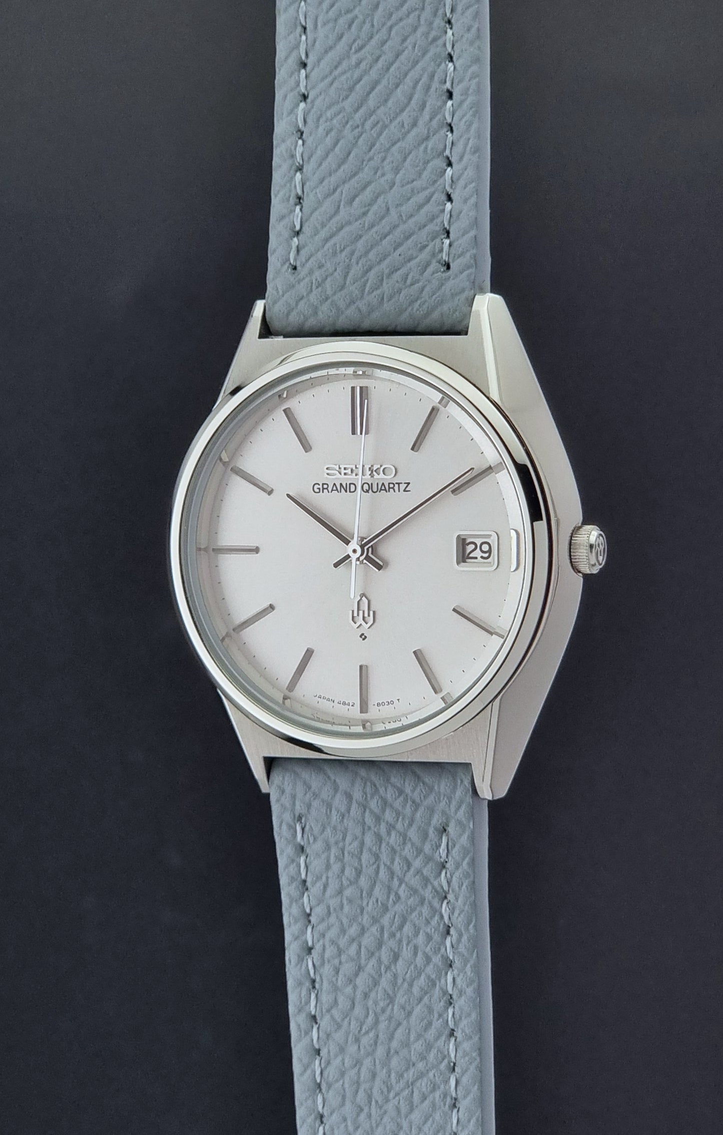 Vintage Seiko Grand Quartz watch 4842-8041 with light grey strap and silver case on a dark gray background crown profile view