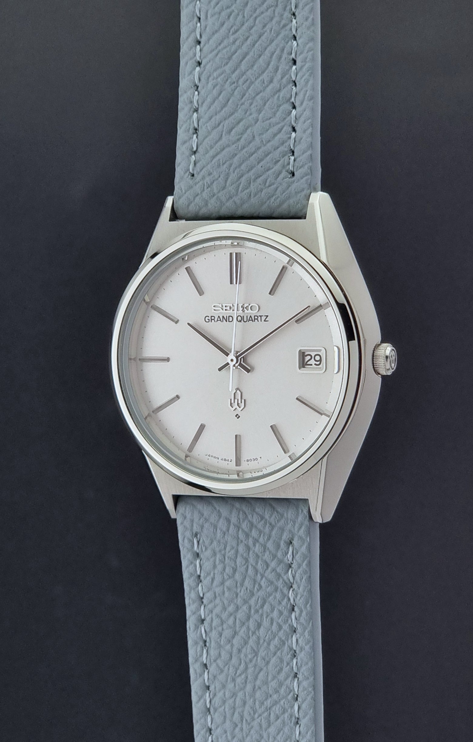 Vintage Seiko Grand Quartz watch 4842-8041 with light grey strap and silver case on a dark gray background crown profile view