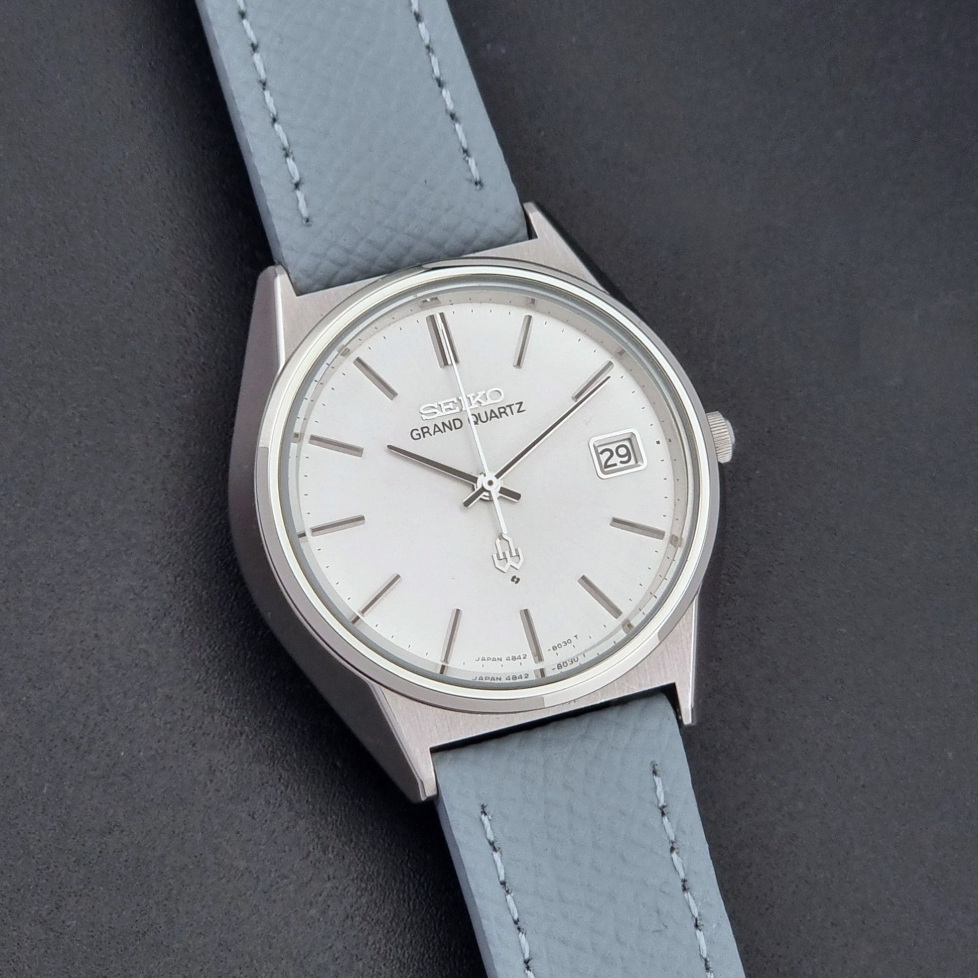 Vintage Seiko Grand Quartz watch 4842-8041 with light grey strap and silver case on a dark gray background close up dial view