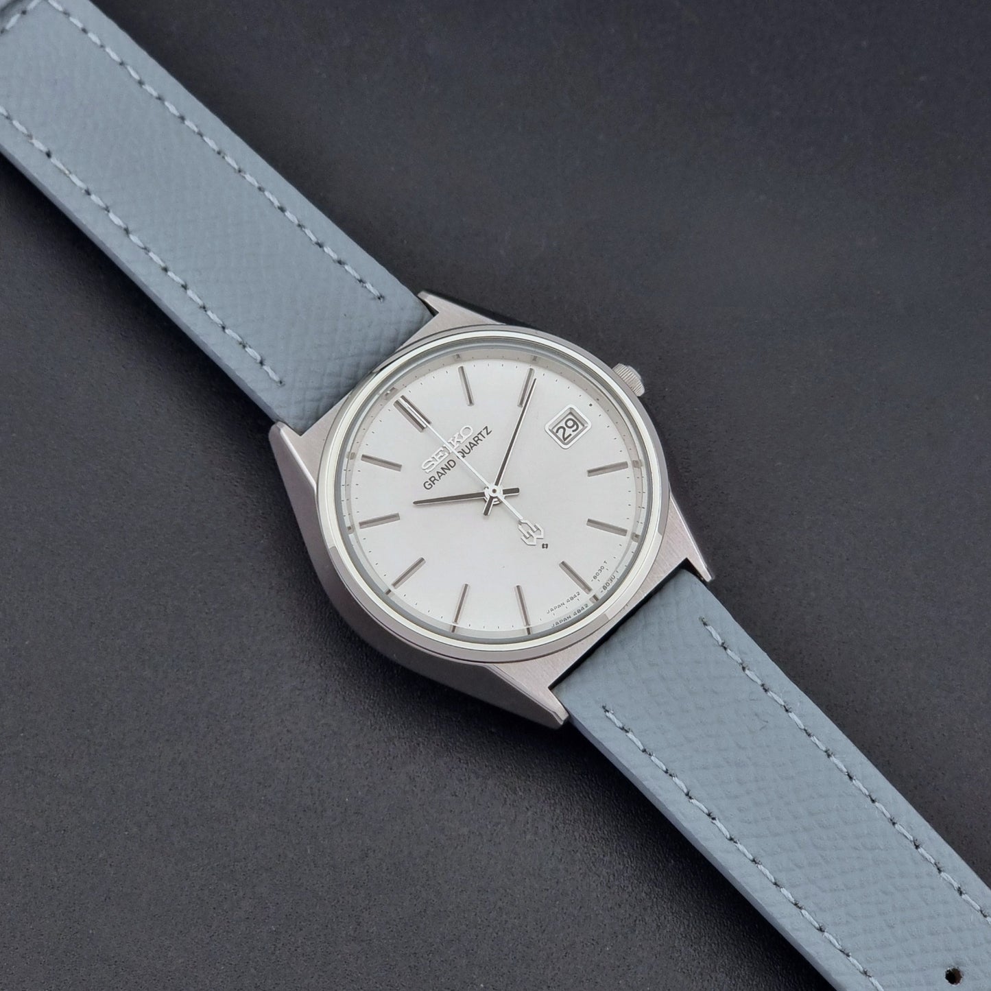 Vintage Seiko Grand Quartz watch 4842-8041 with light grey strap and silver case on a dark gray background front view