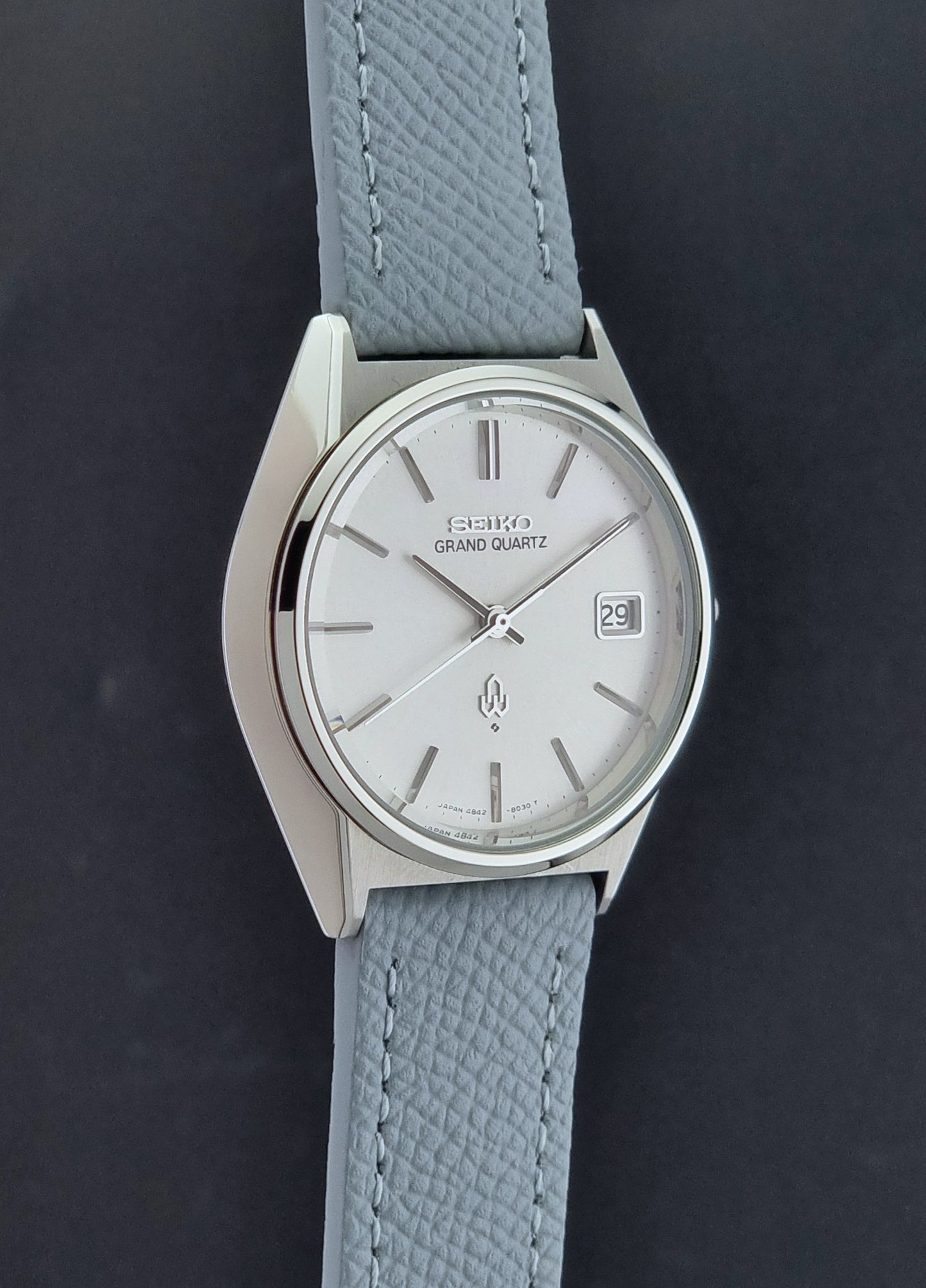 Vintage Seiko Grand Quartz watch 4842-8041 with light grey strap and silver case on a dark gray background side profile view