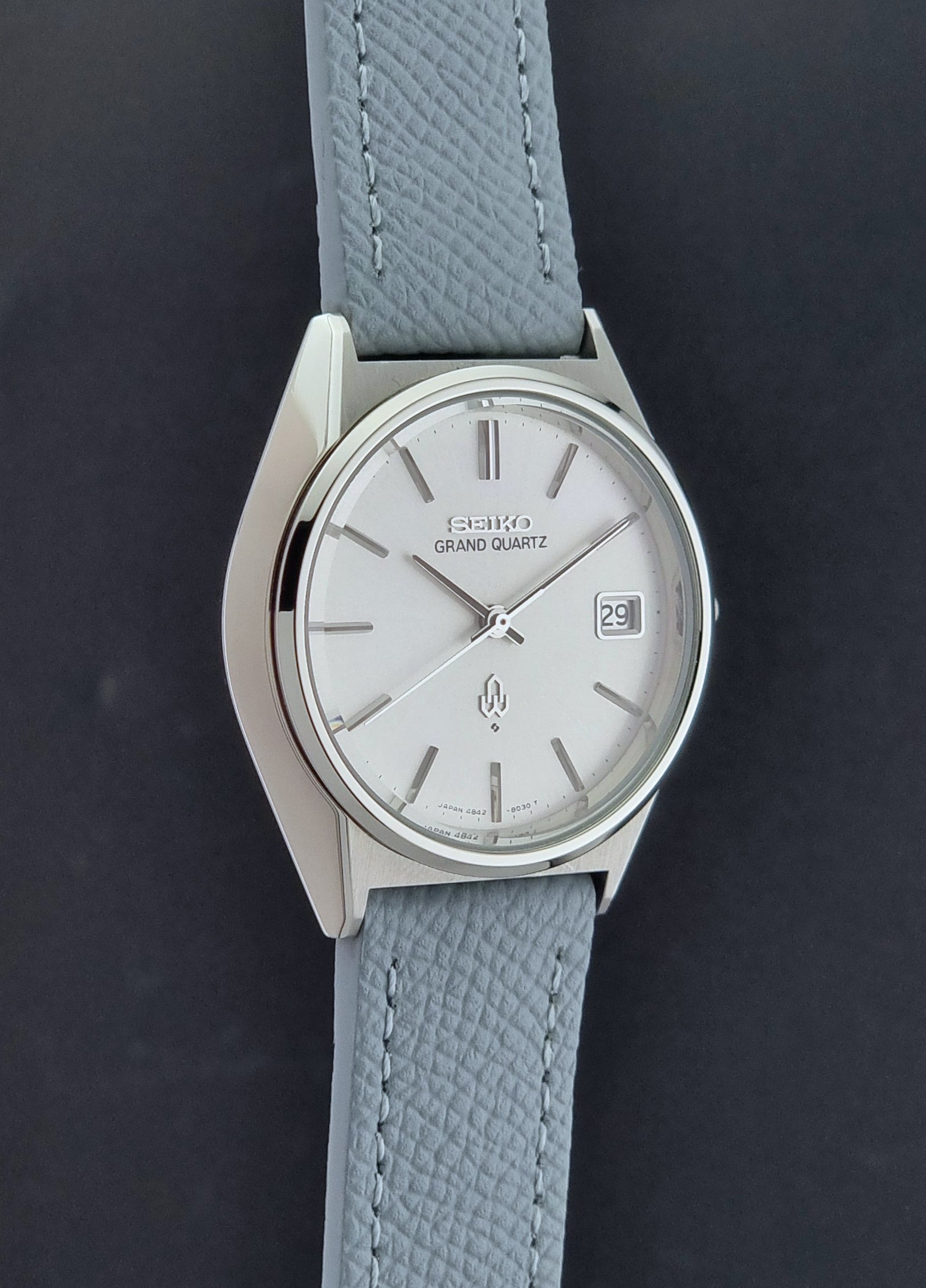 Vintage Seiko Grand Quartz watch 4842-8041 with light grey strap and silver case on a dark gray background side profile view
