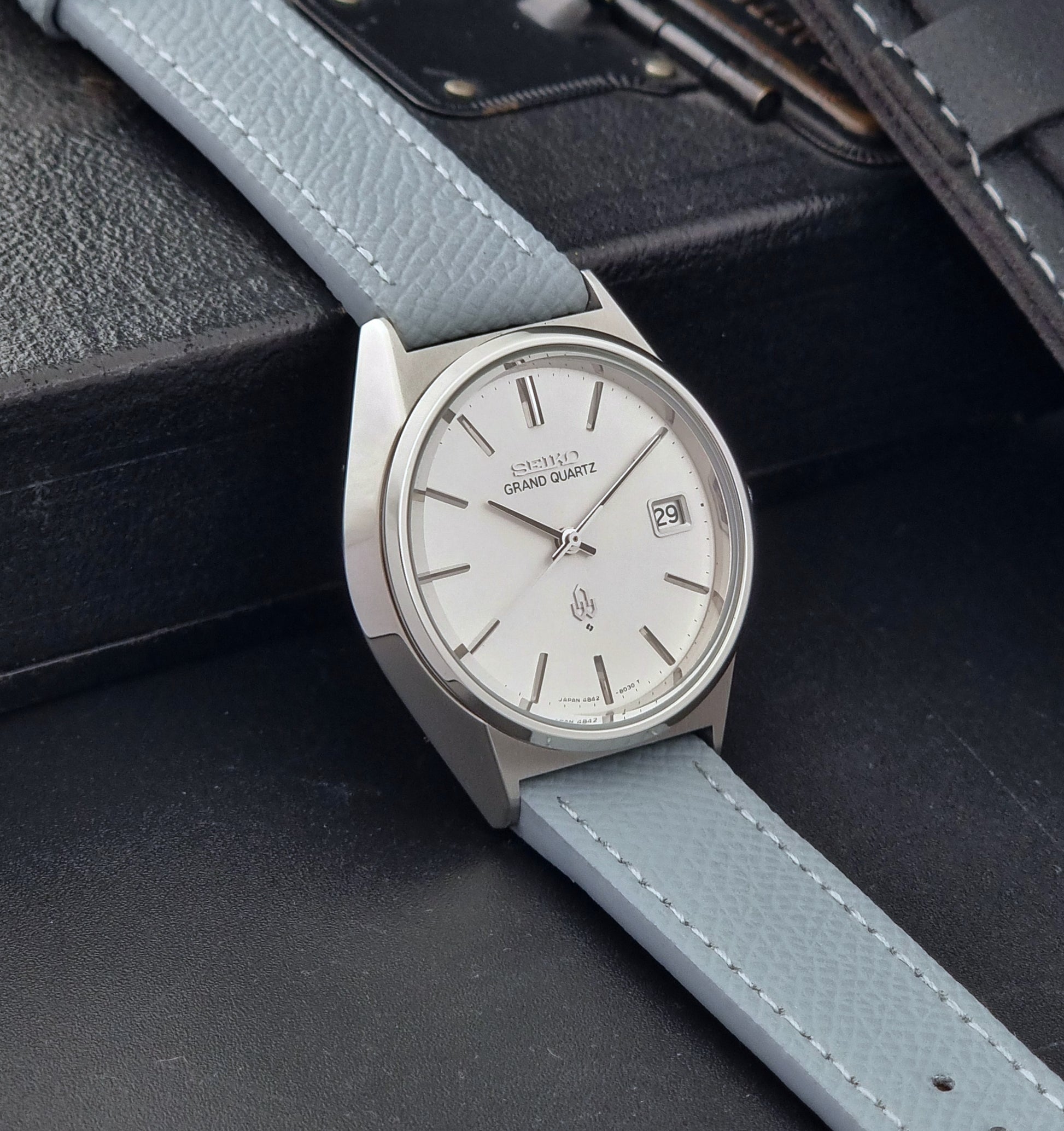 Vintage Seiko Grand Quartz watch 4842-8041 with light grey strap and silver case on a dark gray background side view