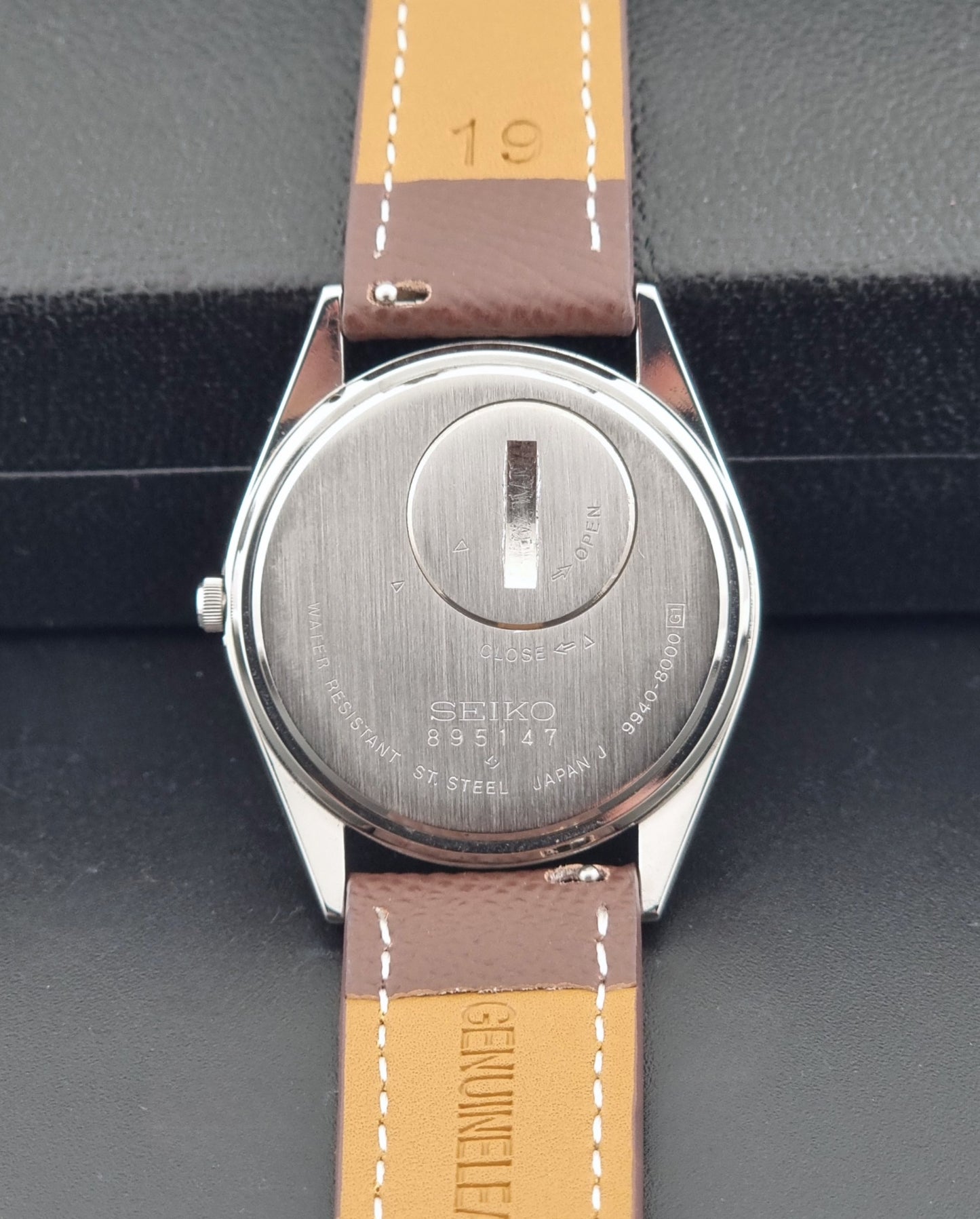 Vintage Seiko Grand Quartz 9940-8000 with a brown textured leather strap on a dark gray background case back view
