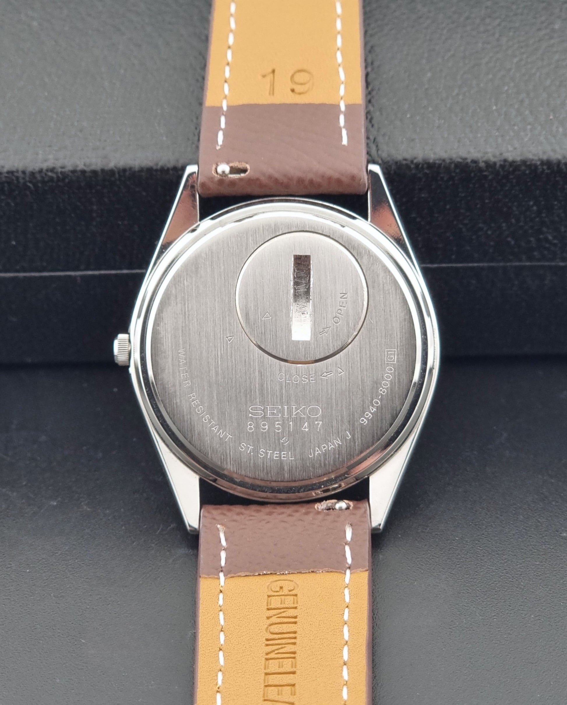 Vintage Seiko Grand Quartz 9940-8000 with a brown textured leather strap on a dark gray background case back view