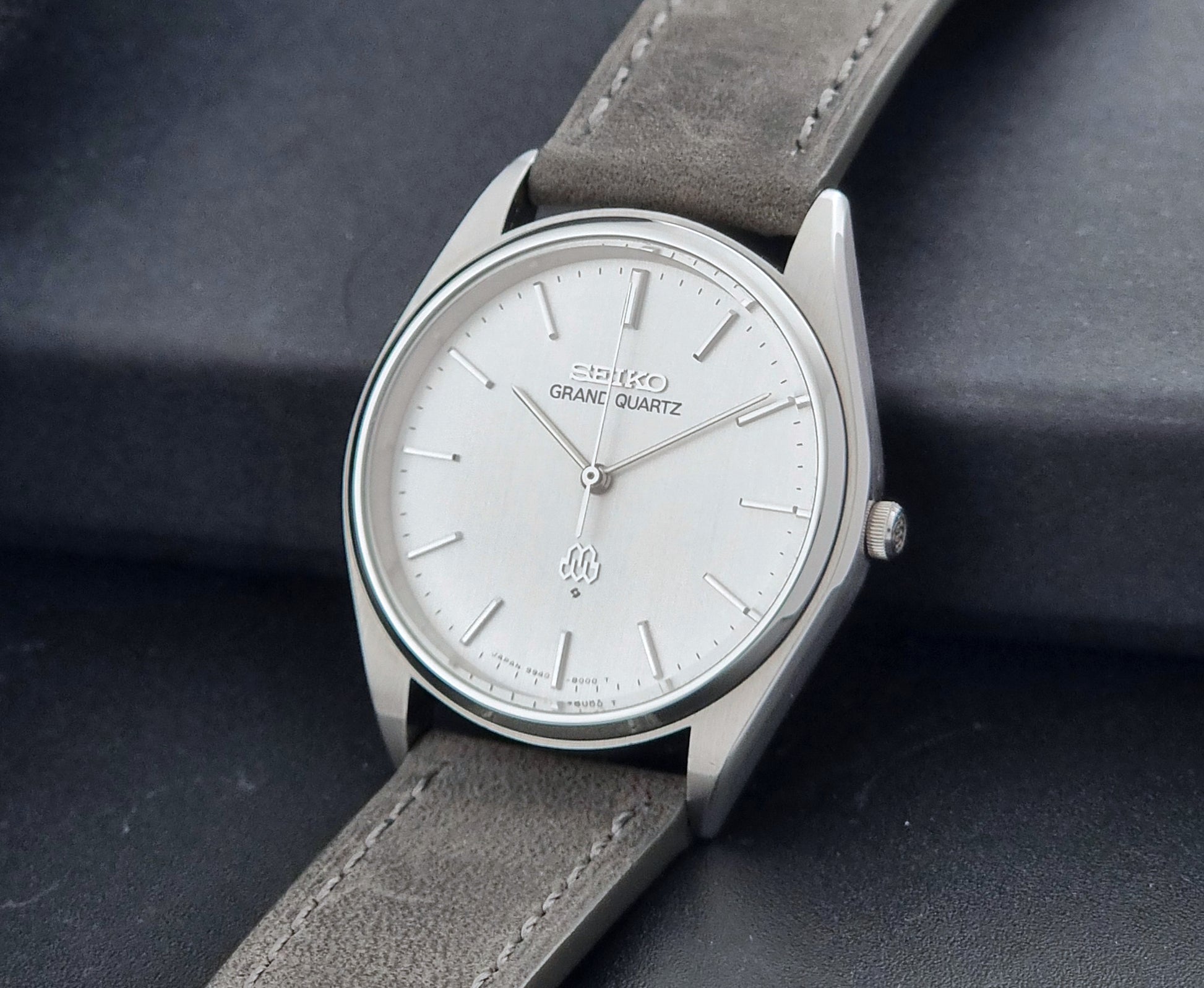 Vintage Seiko Grand Quartz 9940-8000 Watch with gray leather strap and white dial on a dark background crown view