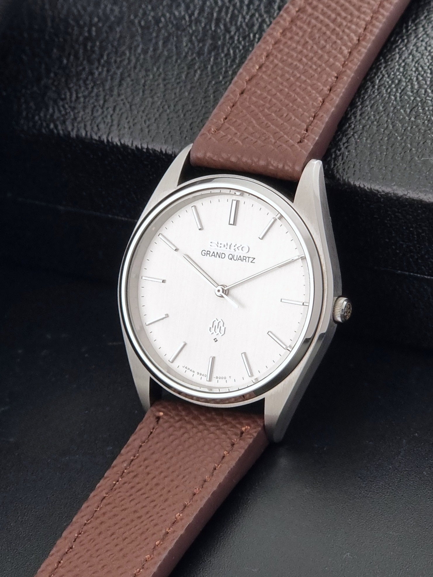 Vintage Seiko Grand Quartz 9940-8000 with a brown textured leather strap on a dark gray background crown view