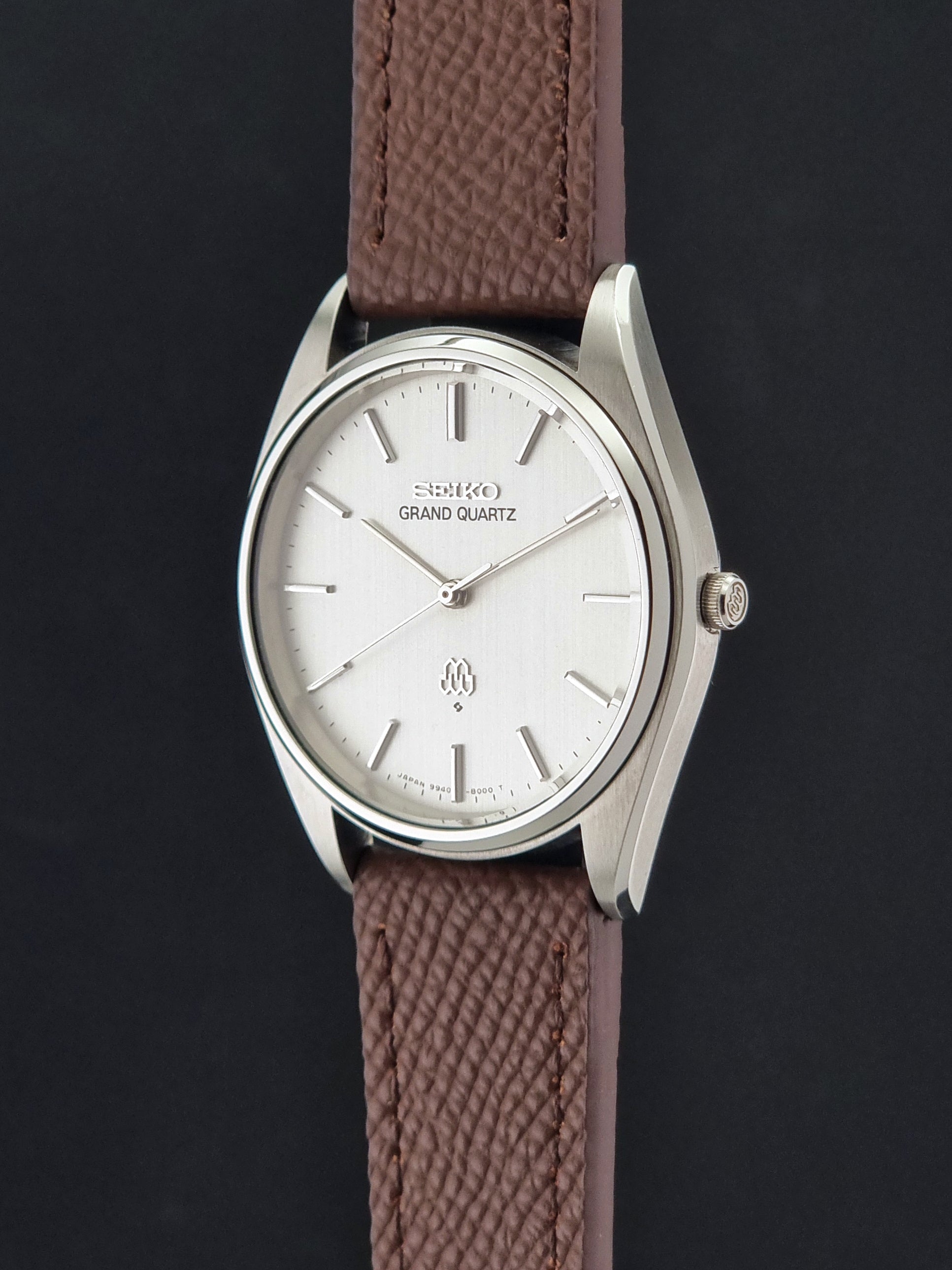 Vintage Seiko Grand Quartz 9940-8000 with a brown textured leather strap on a dark gray background crown profile view