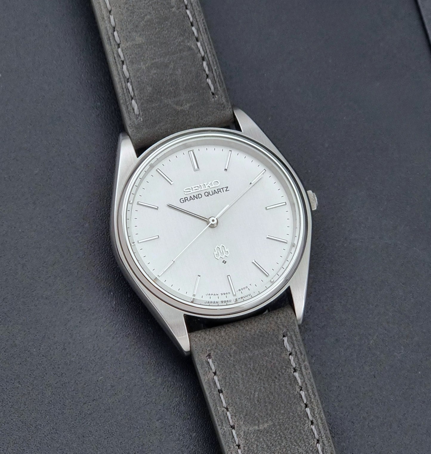 Vintage Seiko Grand Quartz 9940-8000 Watch with gray leather strap and white dial on a dark background front view