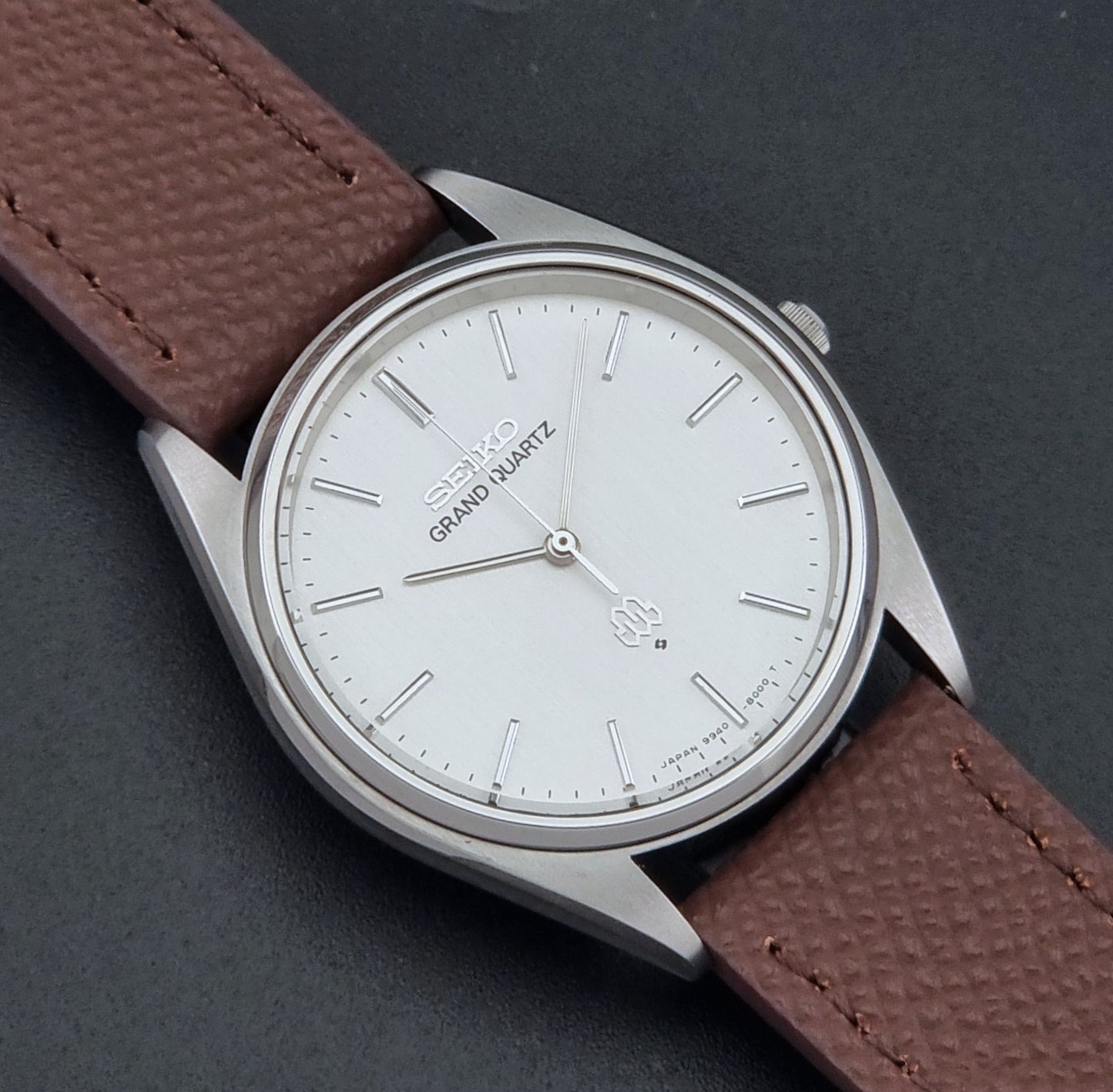 Vintage Seiko Grand Quartz 9940-8000 with a brown textured leather strap on a dark gray background close up dial view