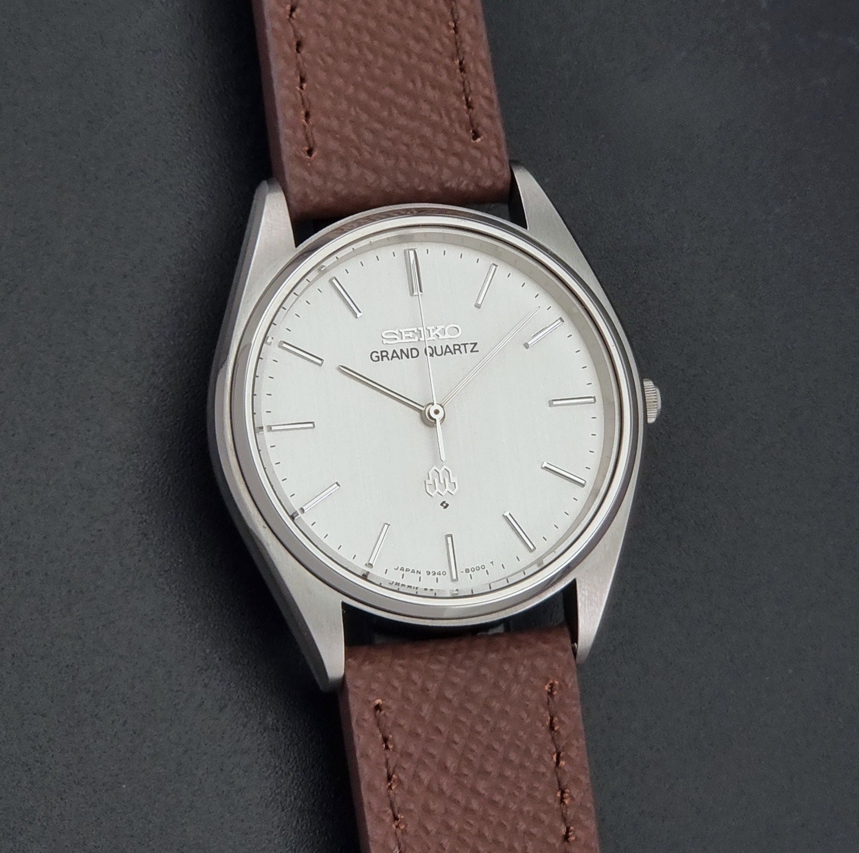 Vintage Seiko Grand Quartz 9940-8000 with a brown textured leather strap on a dark gray background front view