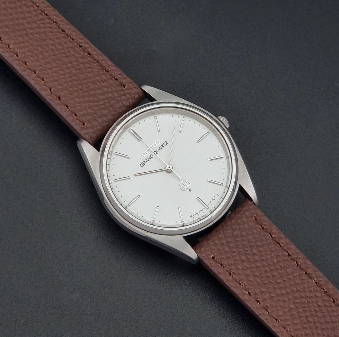 Vintage Seiko Grand Quartz 9940-8000 with a brown textured leather strap on a dark gray background dial