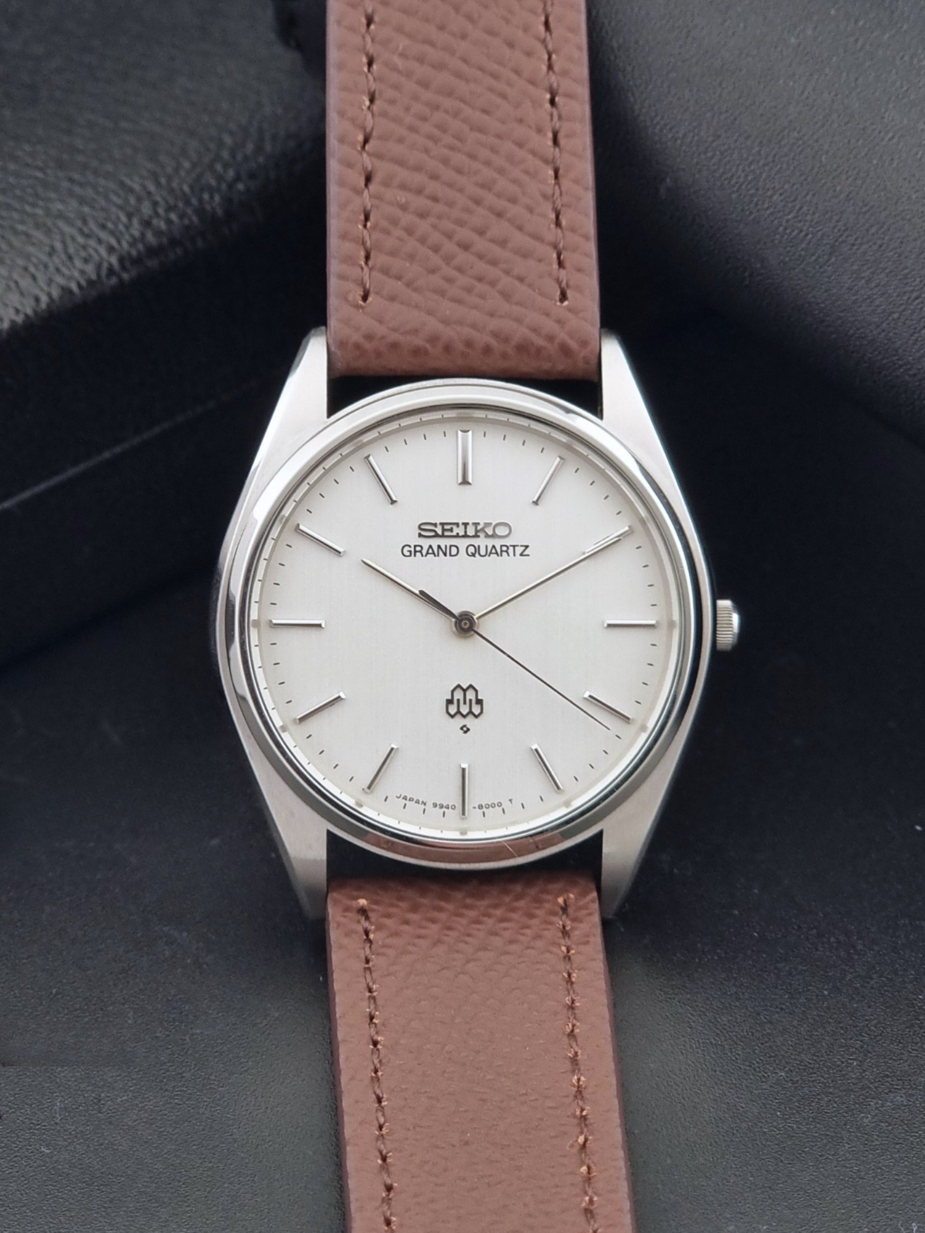 Vintage Seiko Grand Quartz 9940-8000 with a brown textured leather strap on a dark gray background dial view