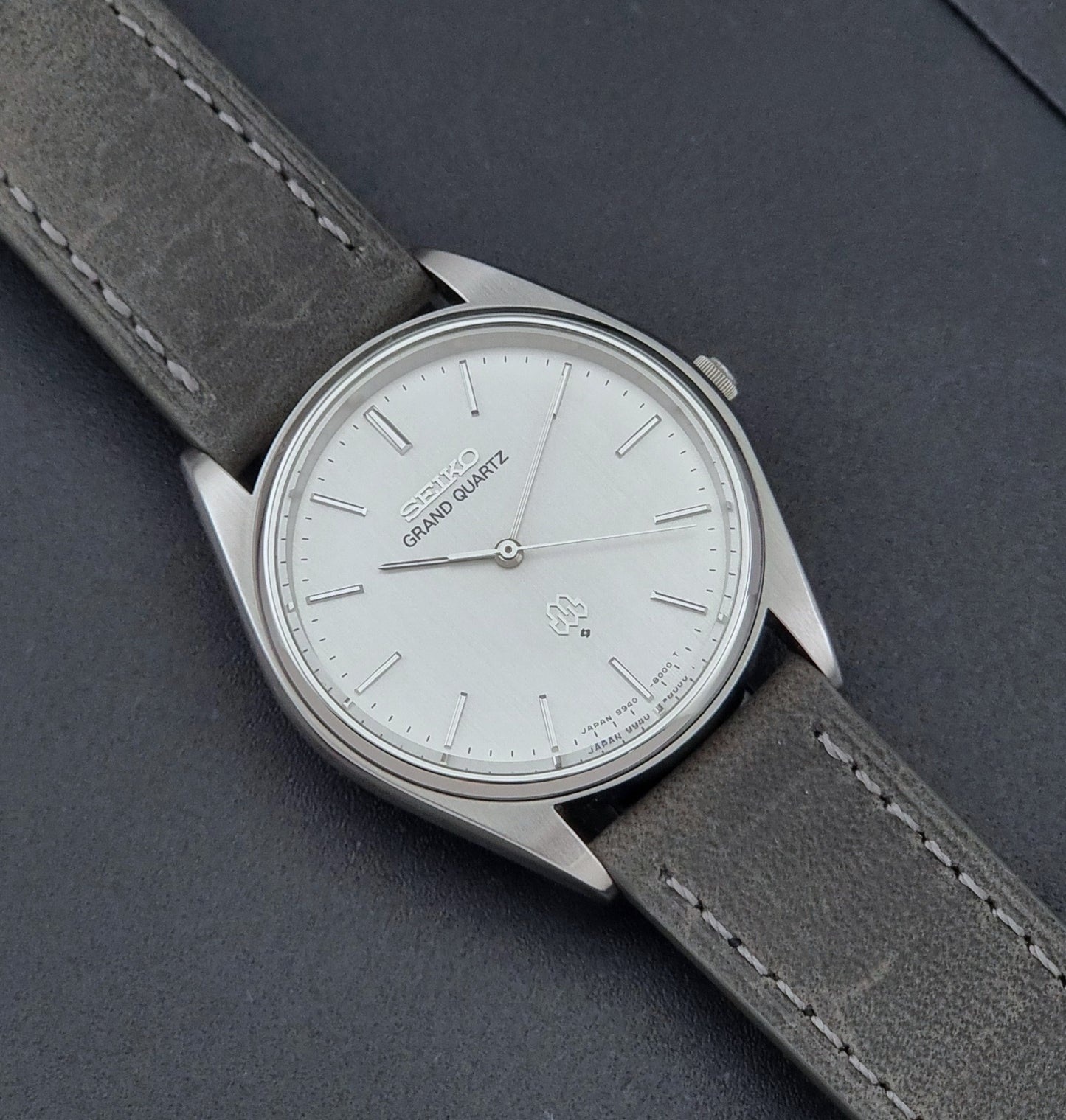 Vintage Seiko Grand Quartz 9940-8000 Watch with gray leather strap and white dial on a dark background close up dial view