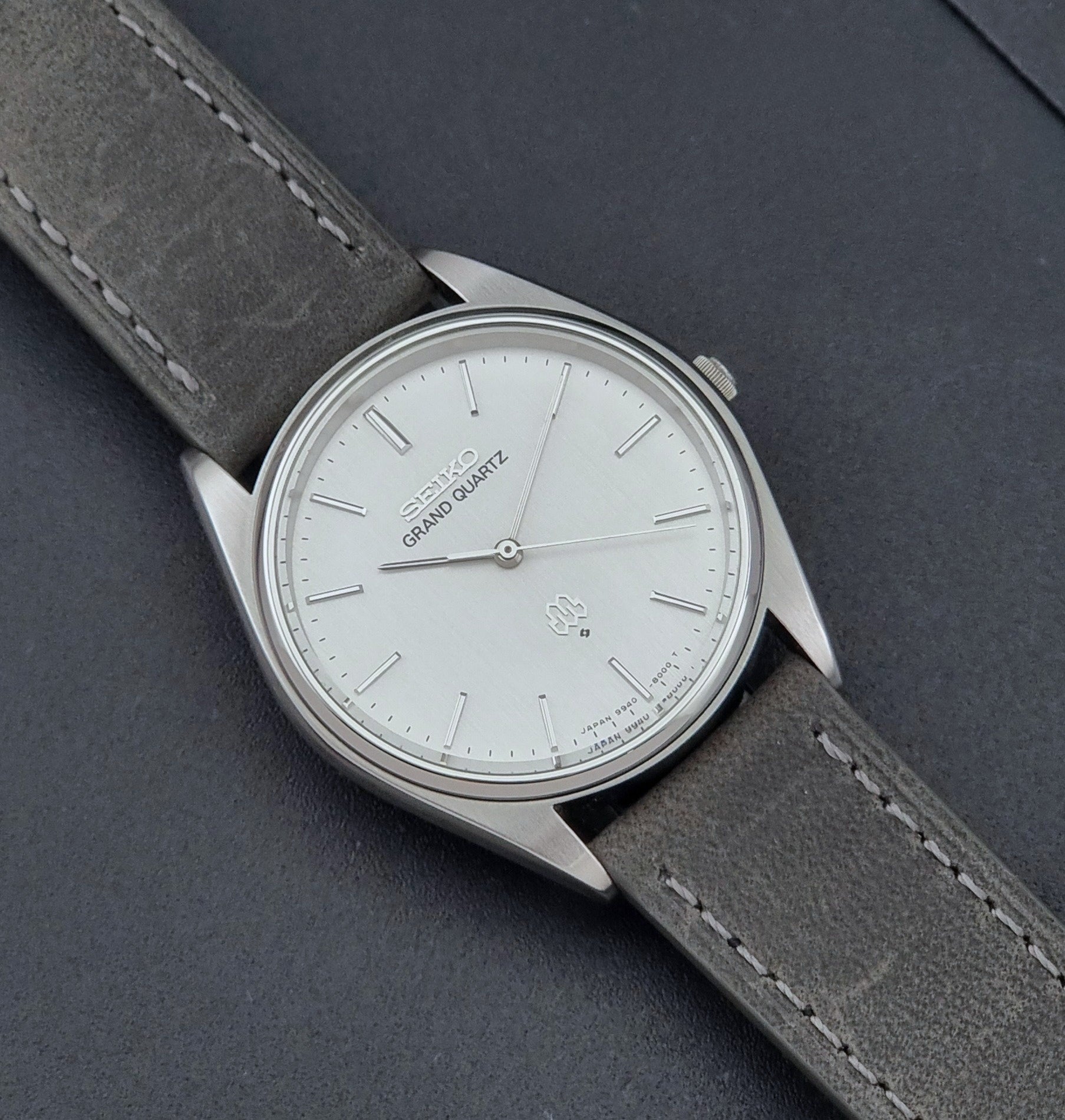 Vintage Seiko Grand Quartz 9940-8000 Watch with gray leather strap and white dial on a dark background close up dial view