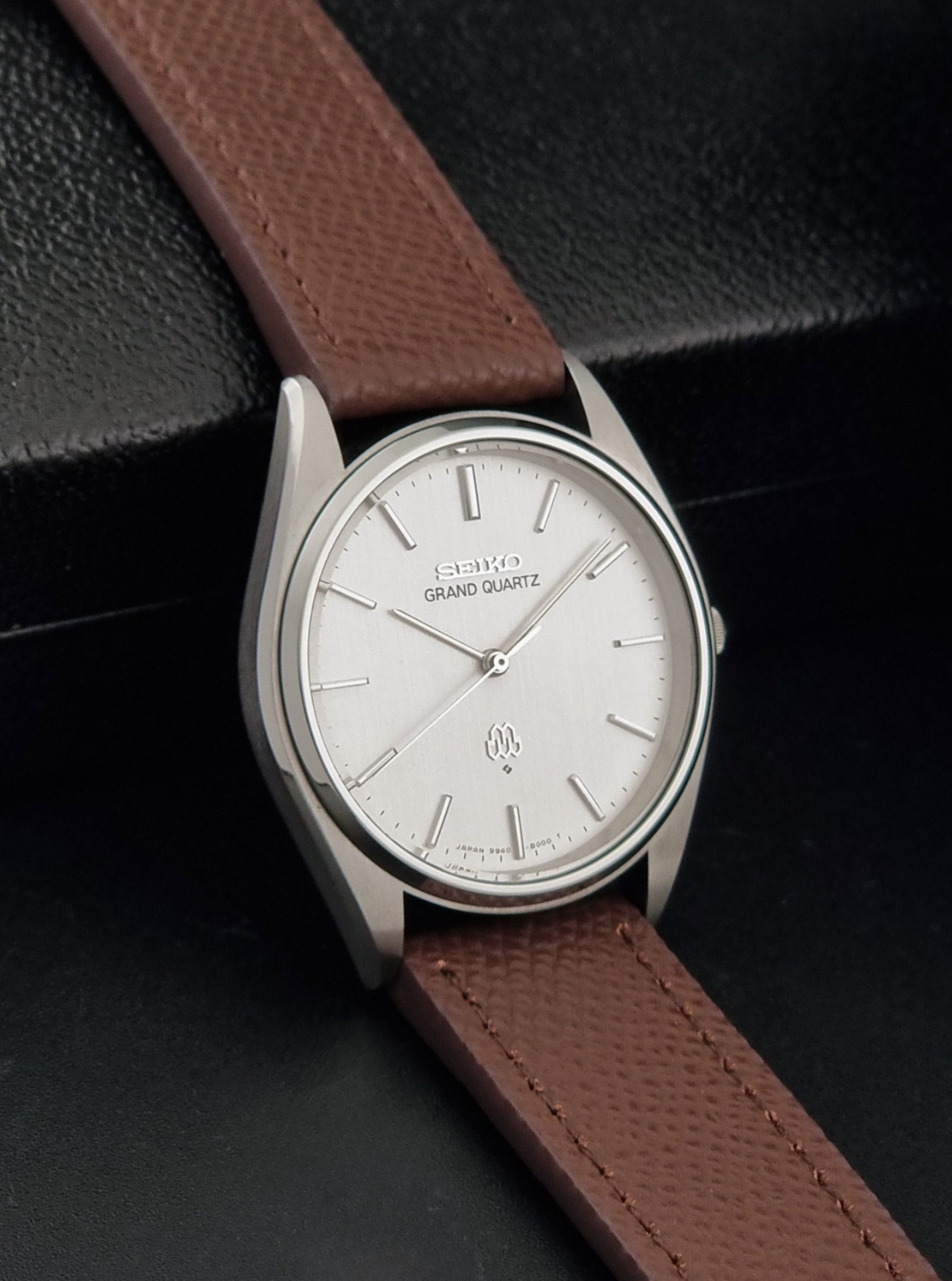 Vintage Seiko Grand Quartz 9940-8000 with a brown textured leather strap on a dark gray background side view