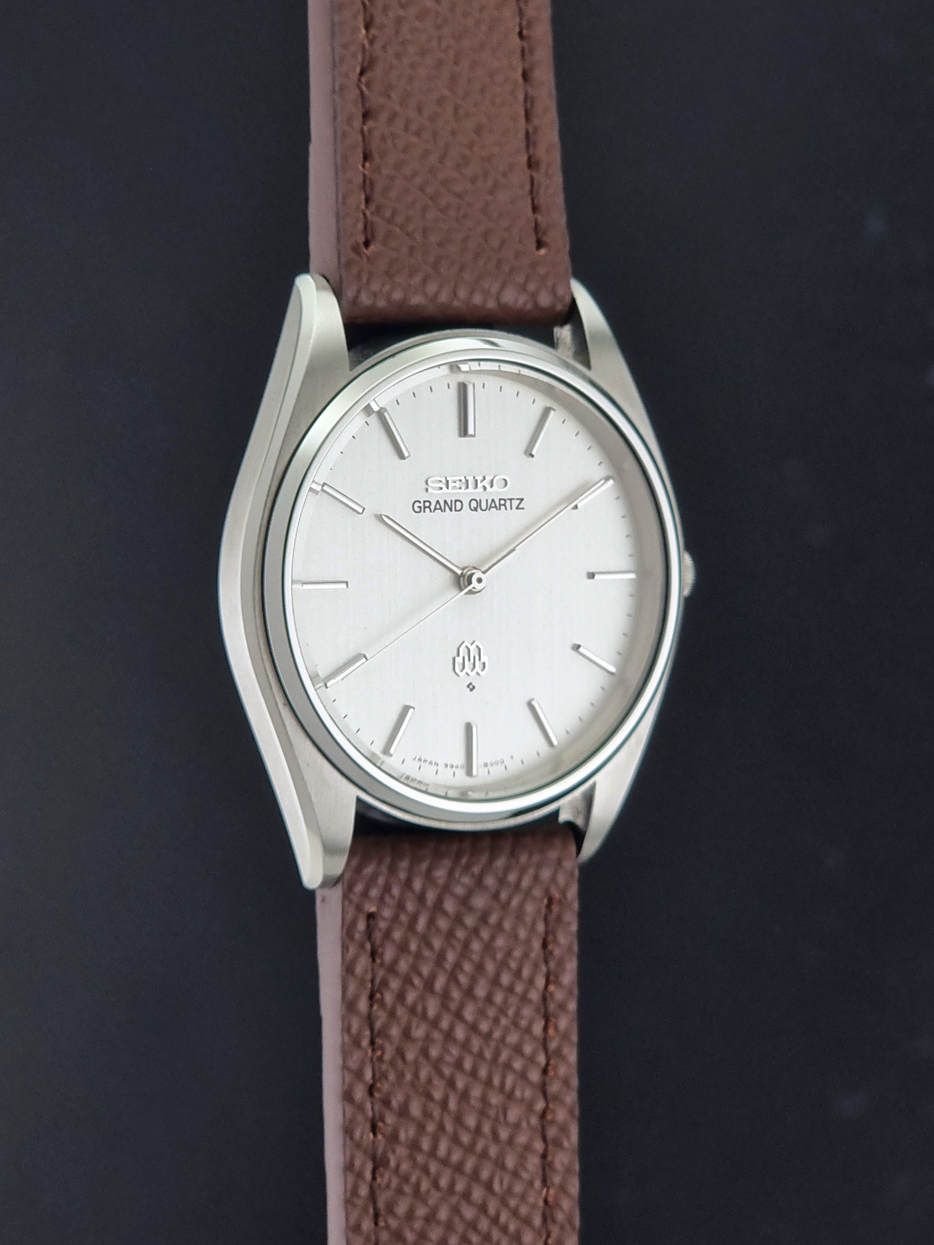 Vintage Seiko Grand Quartz 9940-8000 with a brown textured leather strap on a dark gray background side profile view