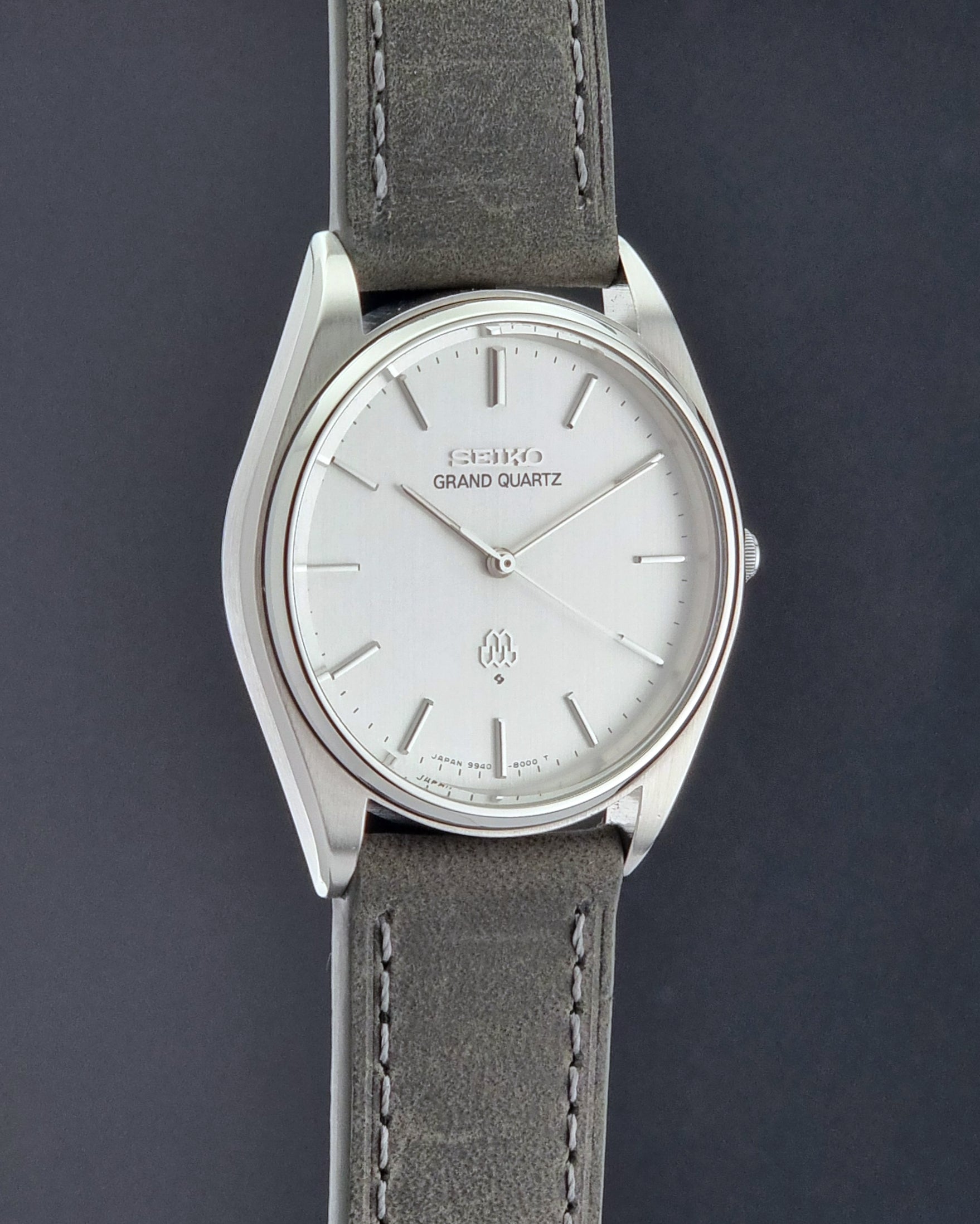 Vintage Seiko Grand Quartz 9940-8000 Watch with gray leather strap and white dial on a dark background side profile view