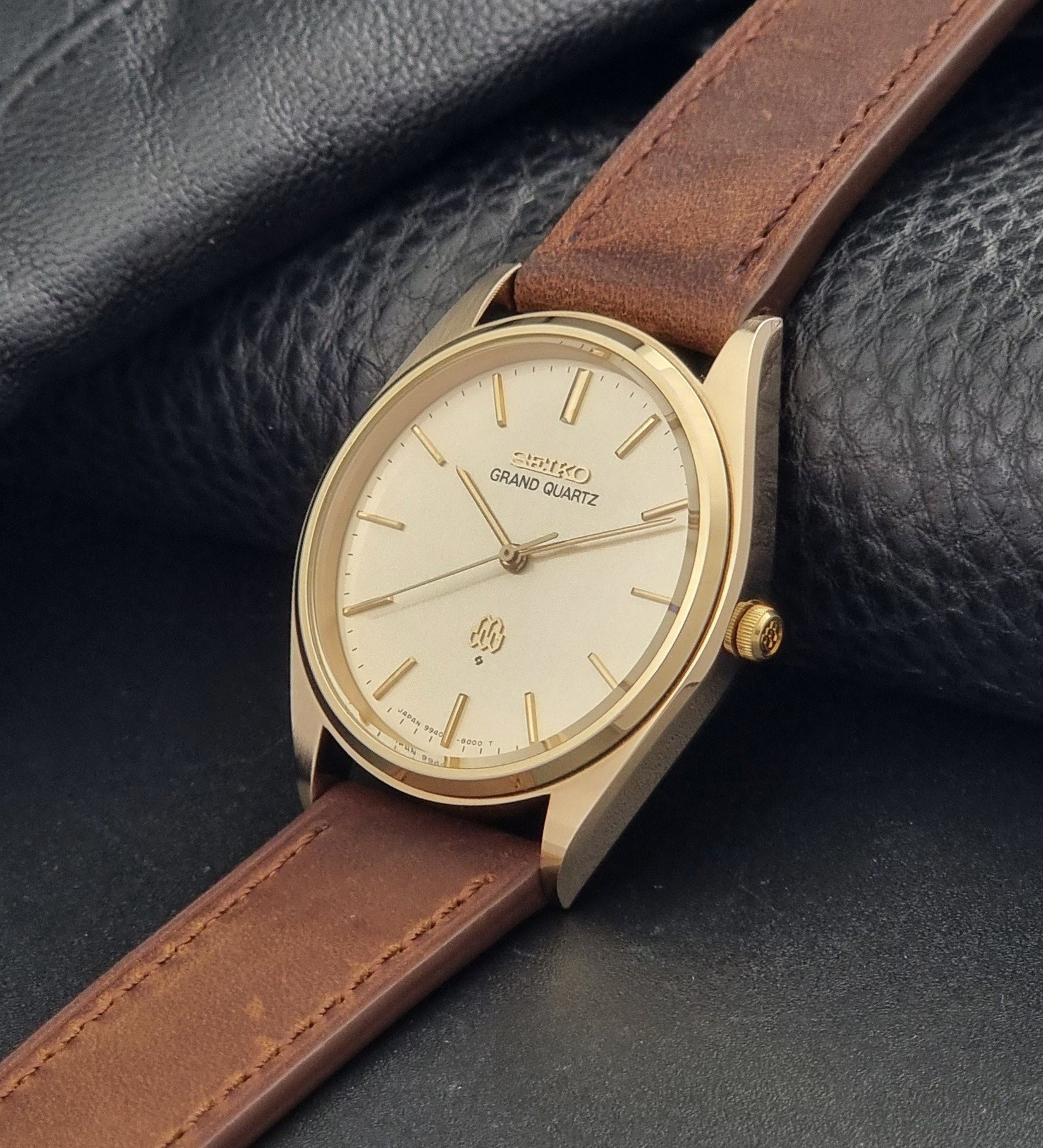 Vintage Seiko Grand Quartz watch 9940-8010 with brown leather strap on a dark textured background close up dial view
