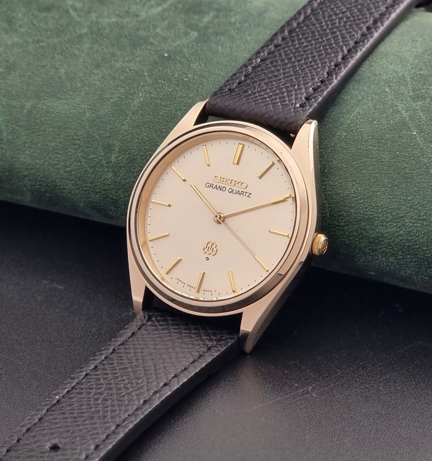 Vintage Seiko Grand Quartz 9940-8010  watch with gold case and black strap on a dark gray background crown view