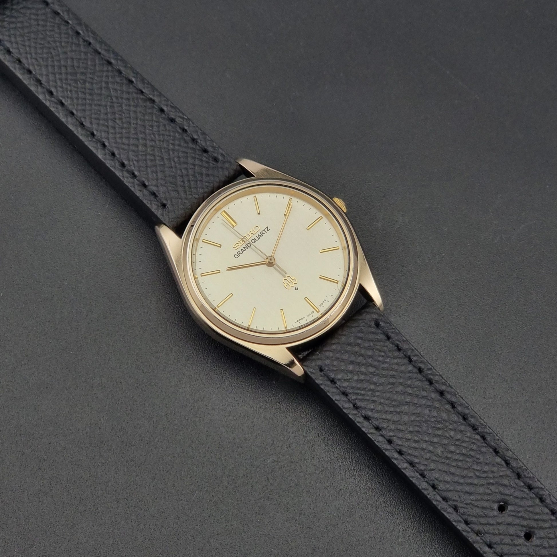 Vintage Seiko Grand Quartz 9940-8010  watch with gold case and black strap on a dark gray background front