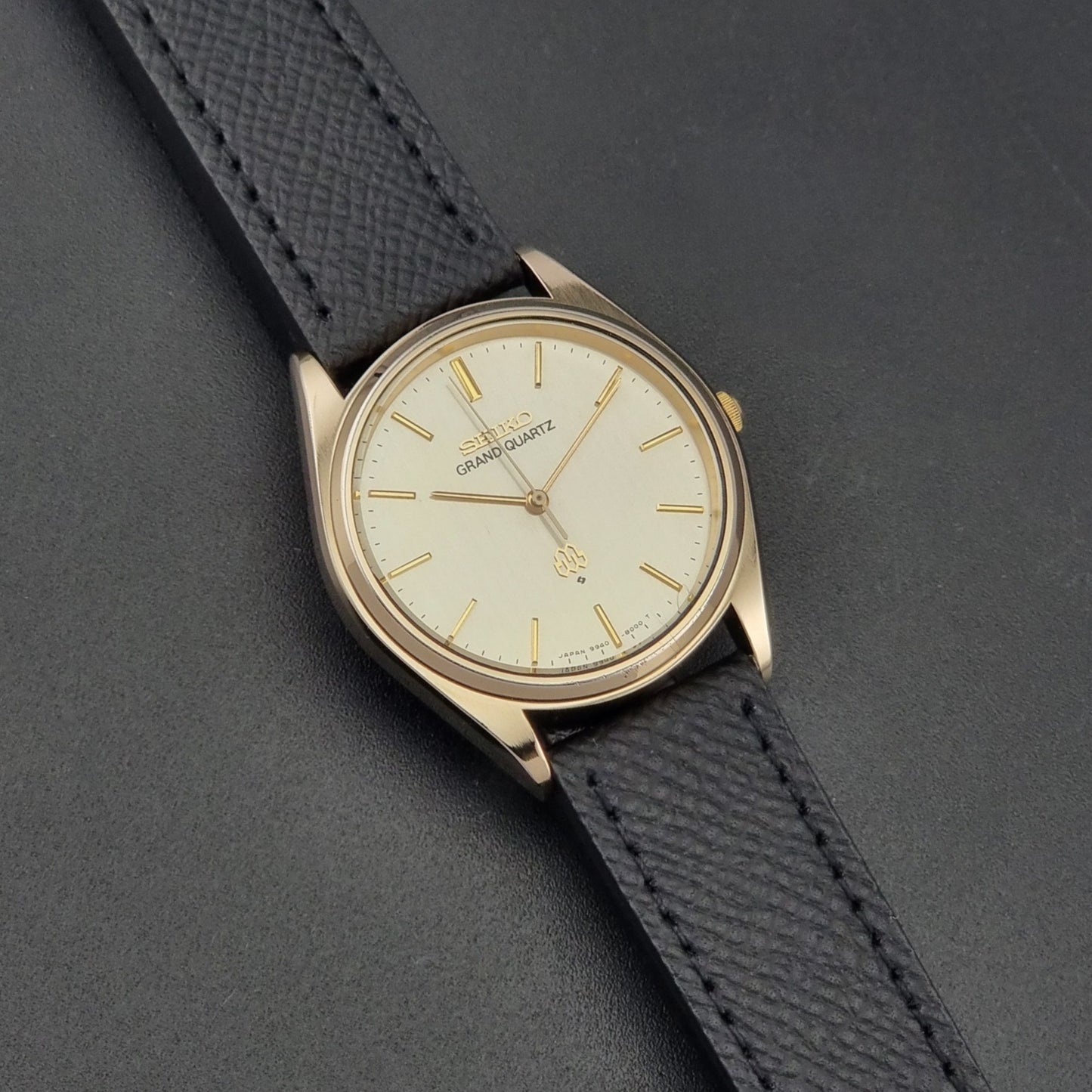 Vintage Seiko Grand Quartz 9940-8010  watch with gold case and black strap on a dark gray background dial view
