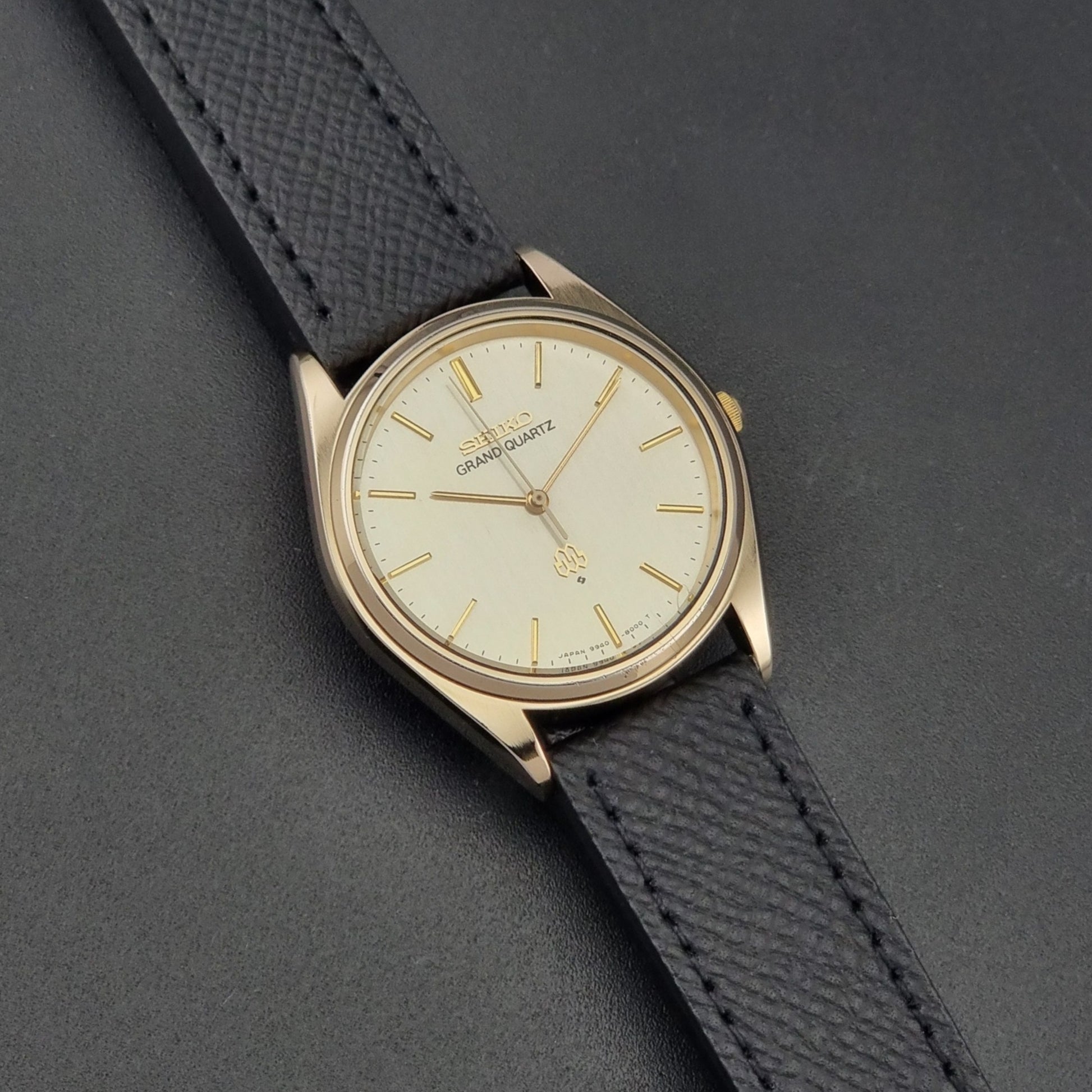 Vintage Seiko Grand Quartz 9940-8010  watch with gold case and black strap on a dark gray background dial view