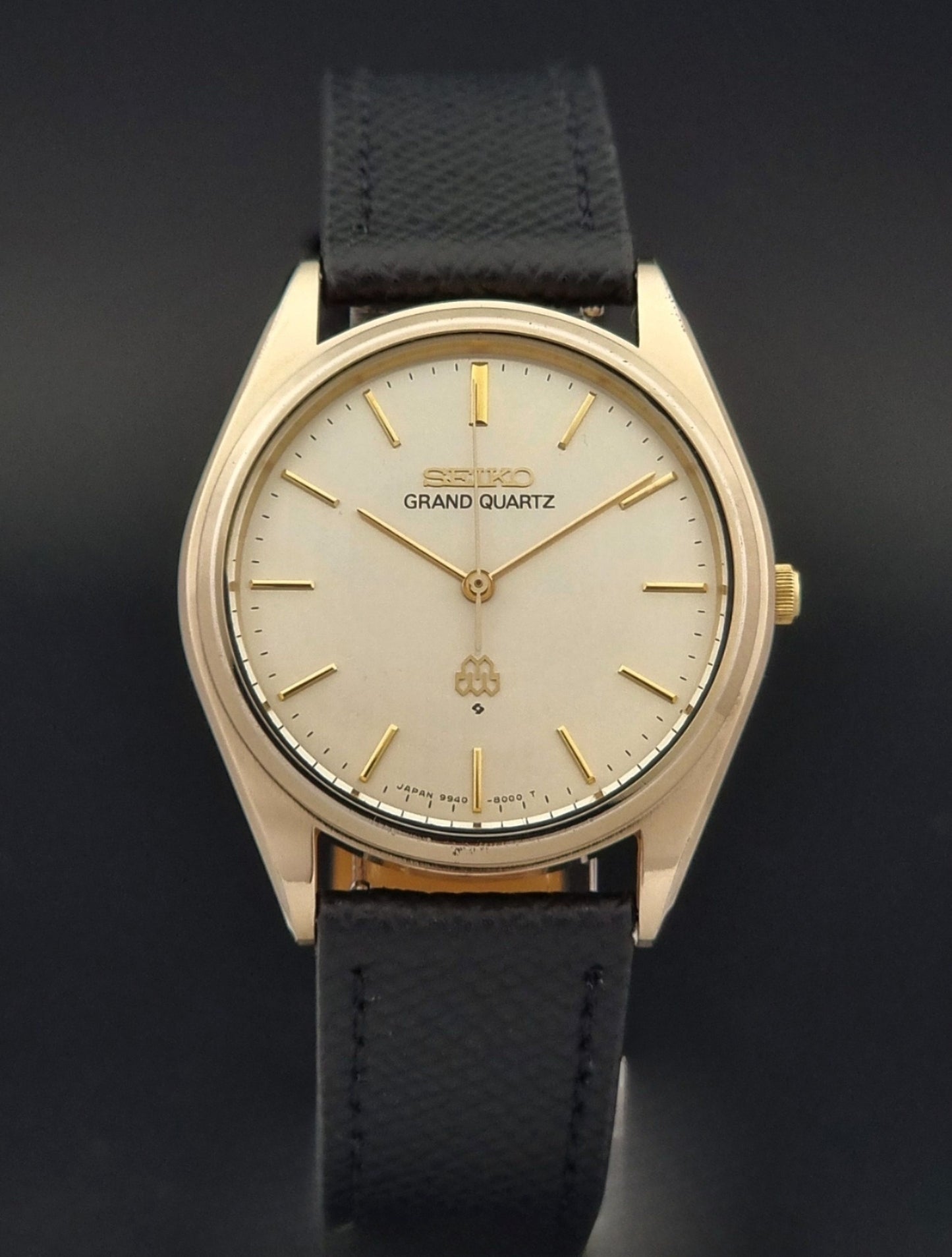 Vintage Seiko Grand Quartz 9940-8010  watch with gold case and black strap on a dark gray background close front view