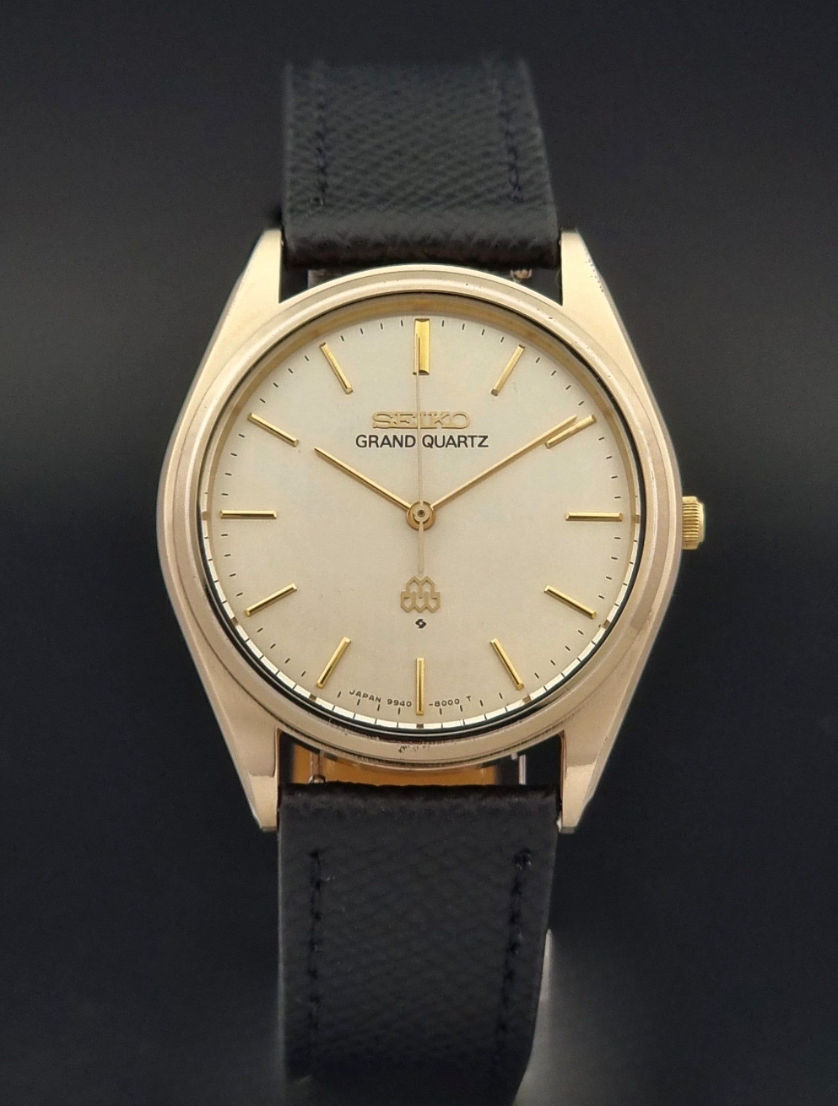 Vintage Seiko Grand Quartz 9940-8010  watch with gold case and black strap on a dark gray background close front view