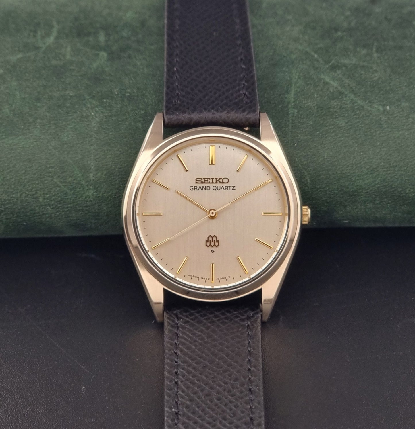 Vintage Seiko Grand Quartz 9940-8010  watch with gold case and black strap on a dark gray background front view