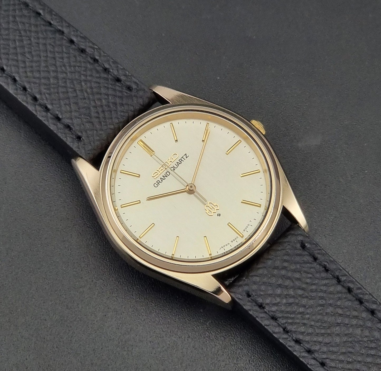 Vintage Seiko Grand Quartz 9940-8010  watch with gold case and black strap on a dark gray background close up dial view