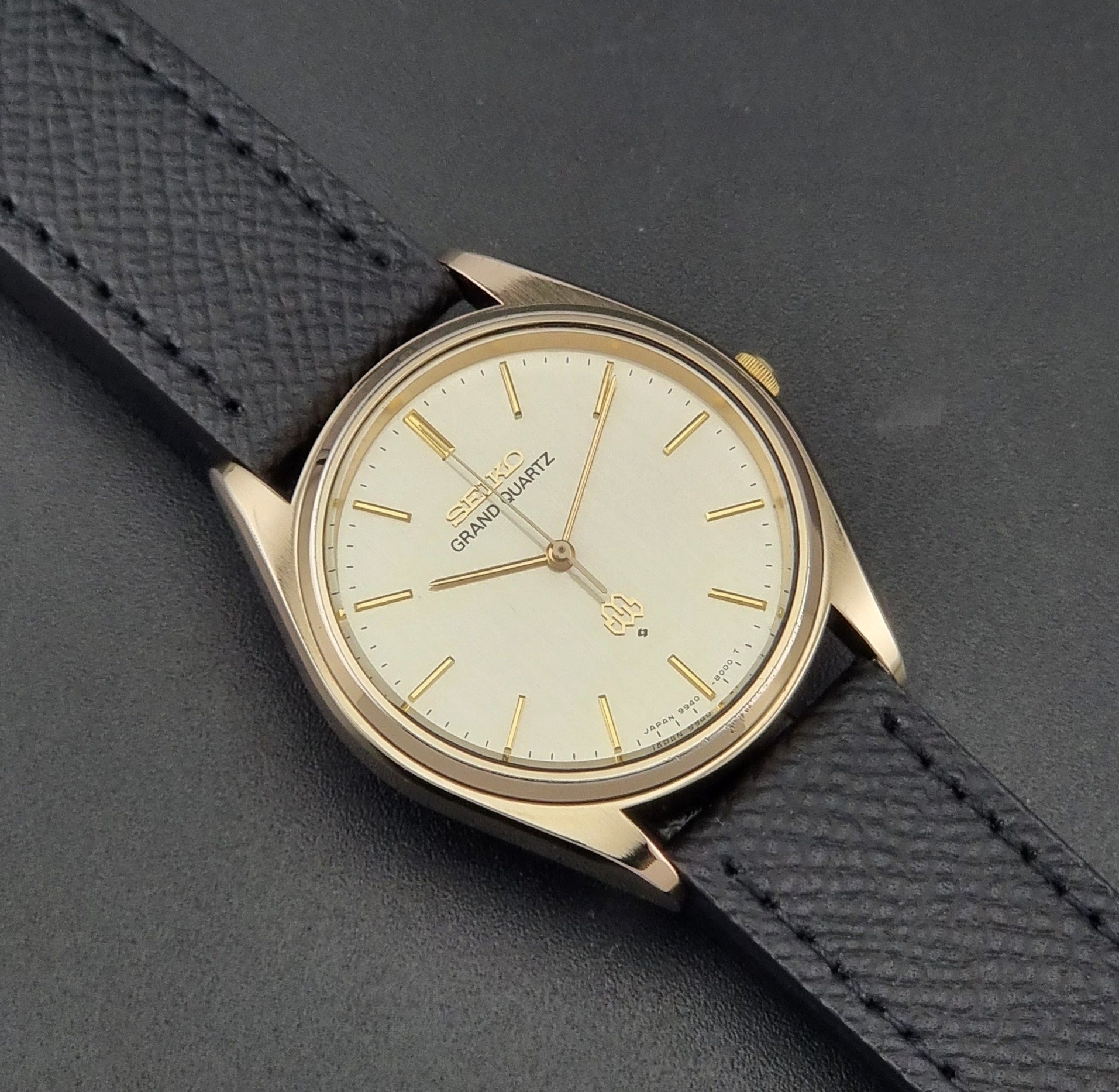 Vintage Seiko Grand Quartz 9940-8010  watch with gold case and black strap on a dark gray background close up dial view