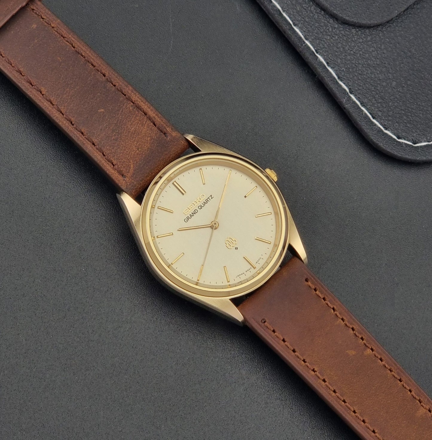 Vintage Seiko Grand Quartz watch 9940-8010 with brown leather strap on a dark textured background dial