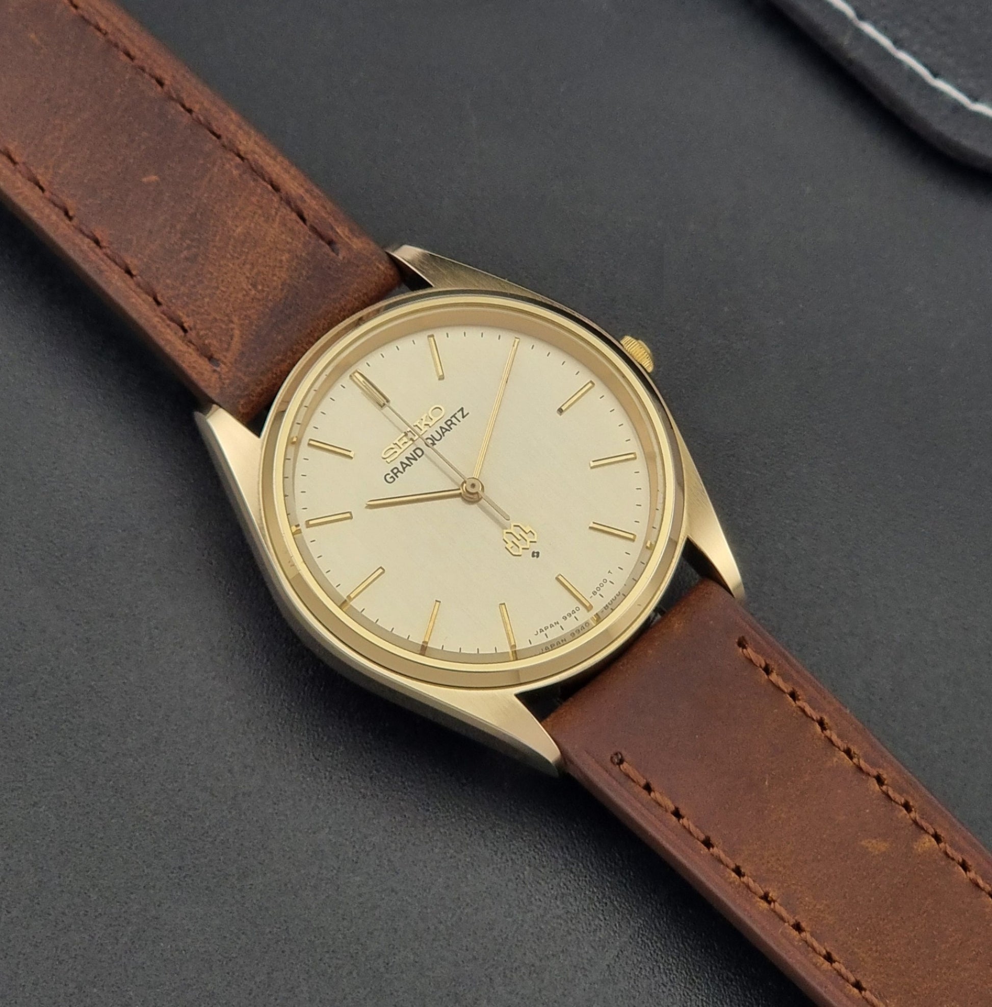Vintage Seiko Grand Quartz watch 9940-8010 with brown leather strap on a dark textured background close dial view