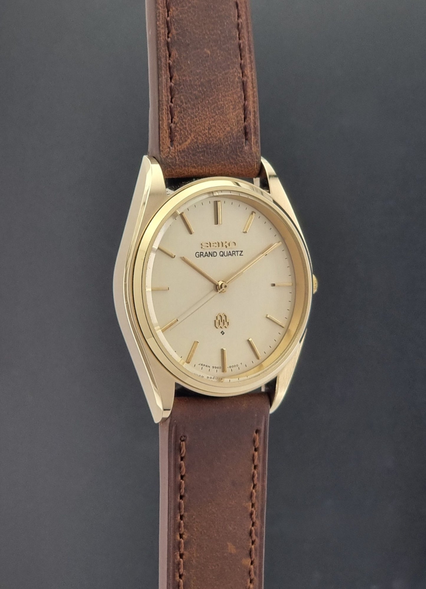 Vintage Seiko Grand Quartz watch 9940-8010 with brown leather strap on a dark textured background side profile view