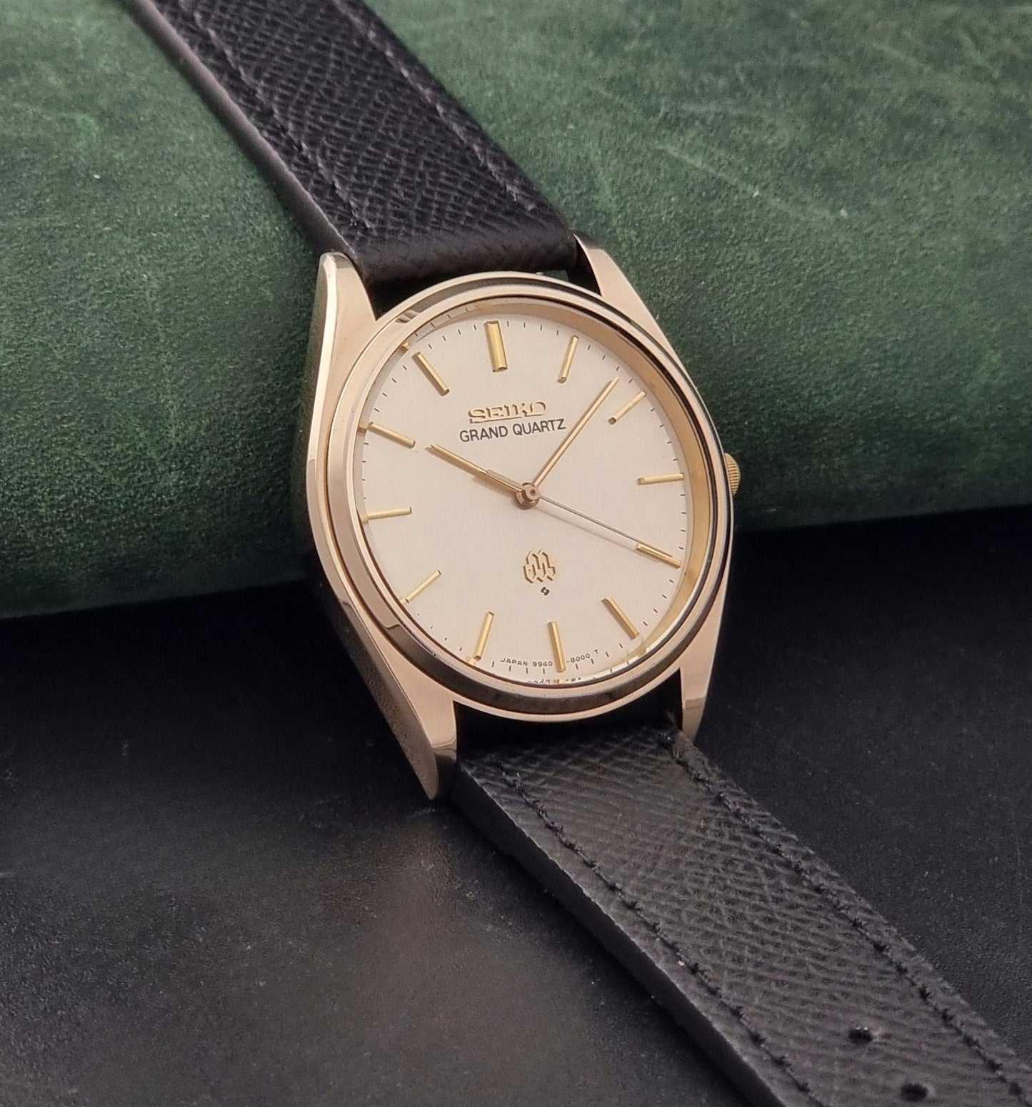 Vintage Seiko Grand Quartz 9940-8010  watch with gold case and black strap on a dark gray background side view