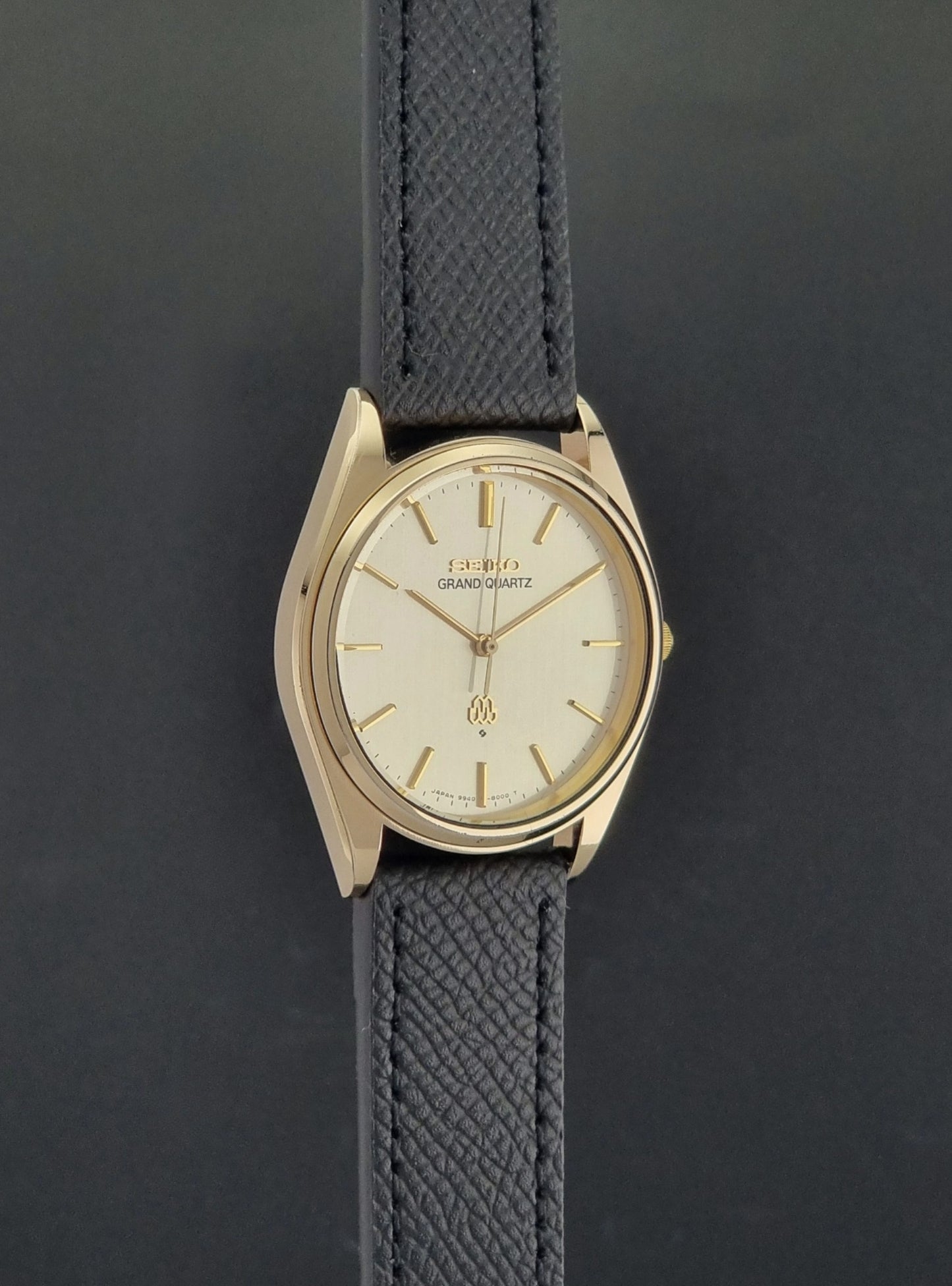 Vintage Seiko Grand Quartz 9940-8010  watch with gold case and black strap on a dark gray background side profile view